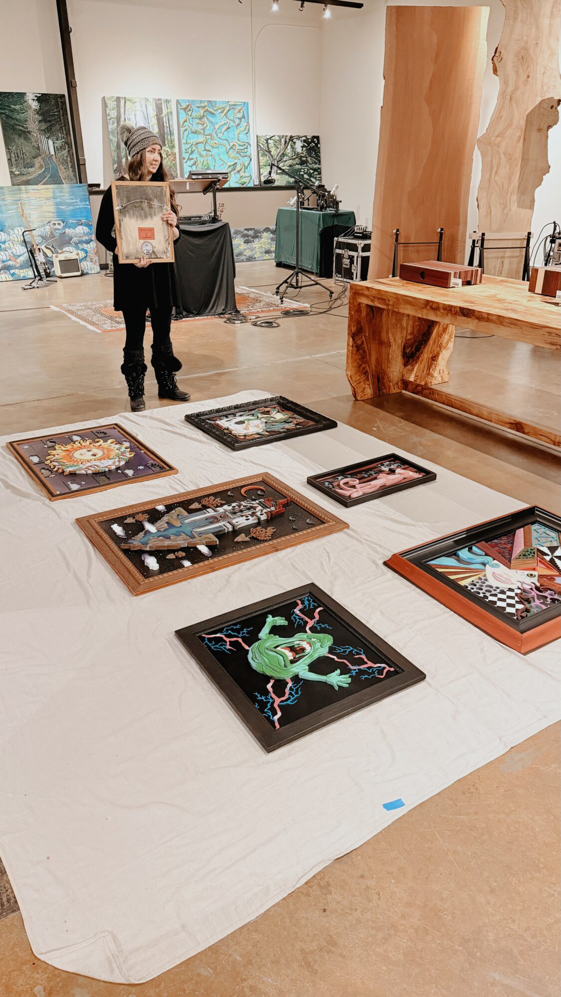 Person standing in art gallery with paintings on the wall and artwork displayed on the floor.