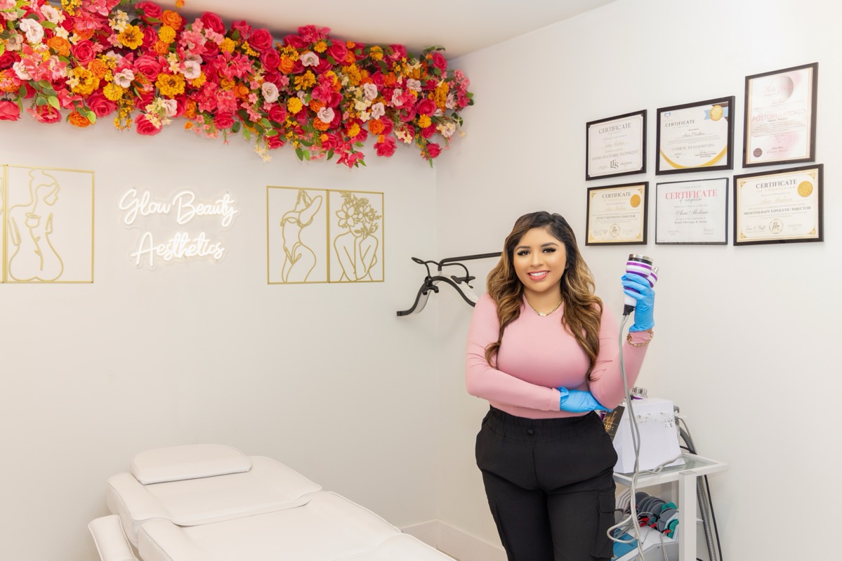 Woman in pink top and black pants holding a water bottle in a room with certificates and floral decorations.