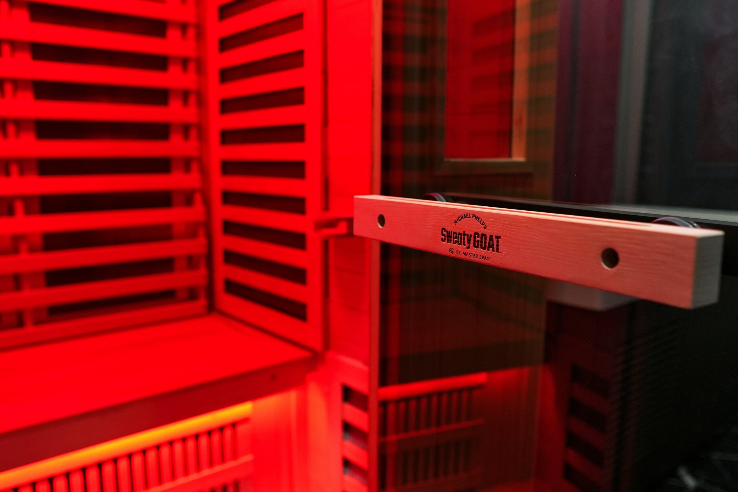 Close-up of a red sauna interior with wooden slats and glass door, illuminated by red lighting.