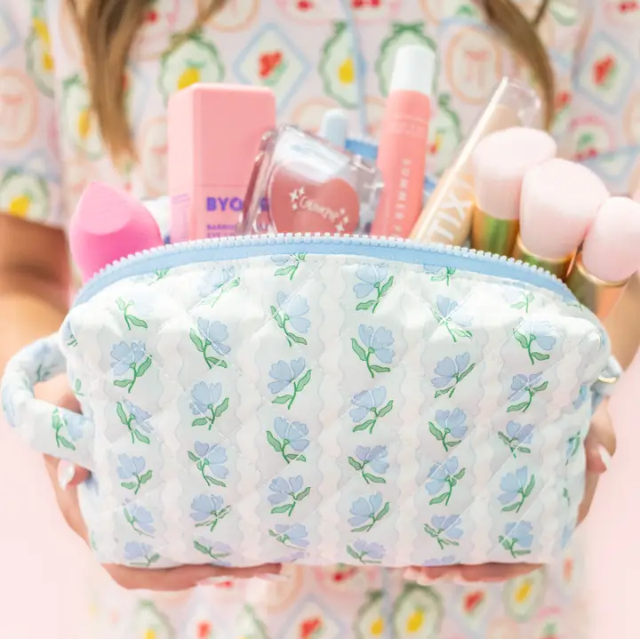 Person holding a floral-patterned bag filled with various skincare and cosmetic products.