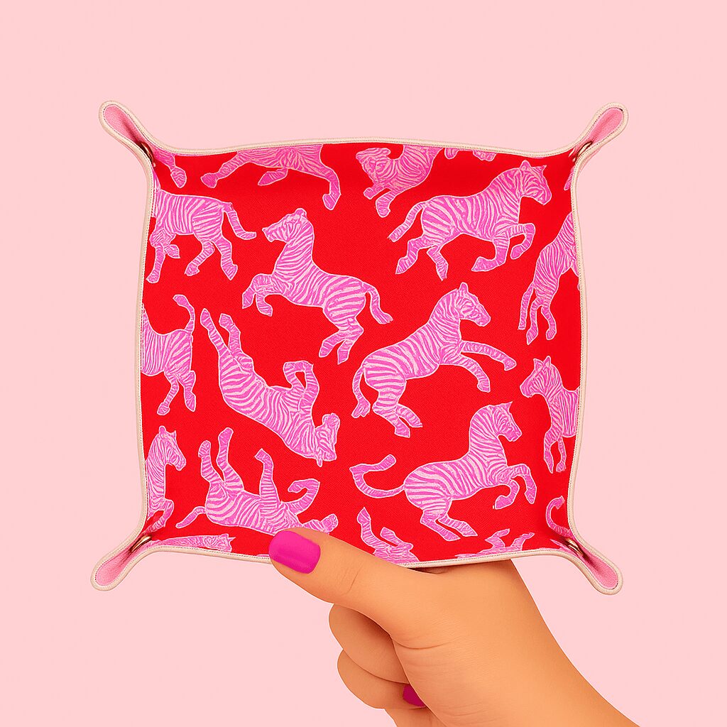 Hand holding a small fabric square with zebra pattern, pink and red colors, against a pink background.