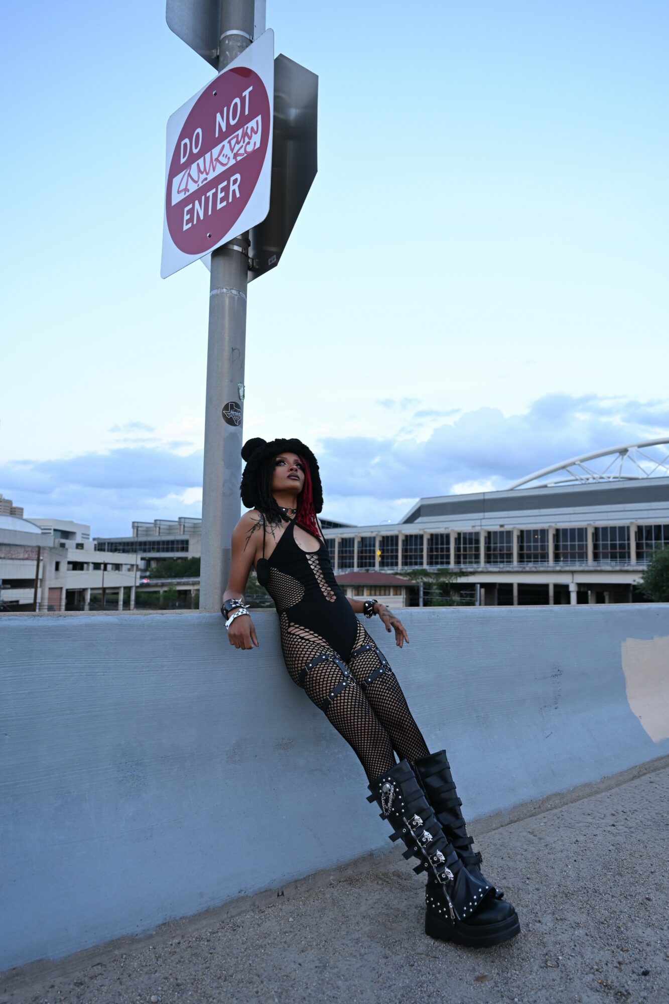 Person leaning against a wall near a do not enter sign, with a large building in the background.