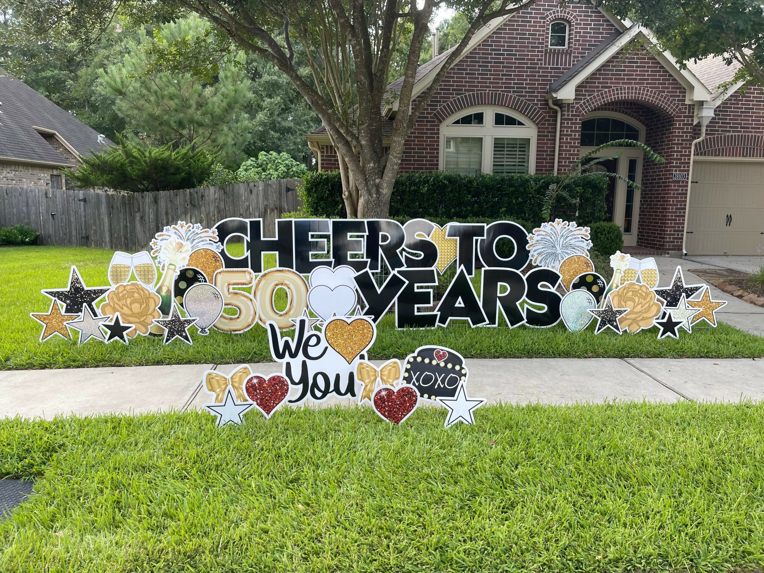 Decorative sign celebrating 50 years with stars, hearts, and text on a lawn in front of a house.