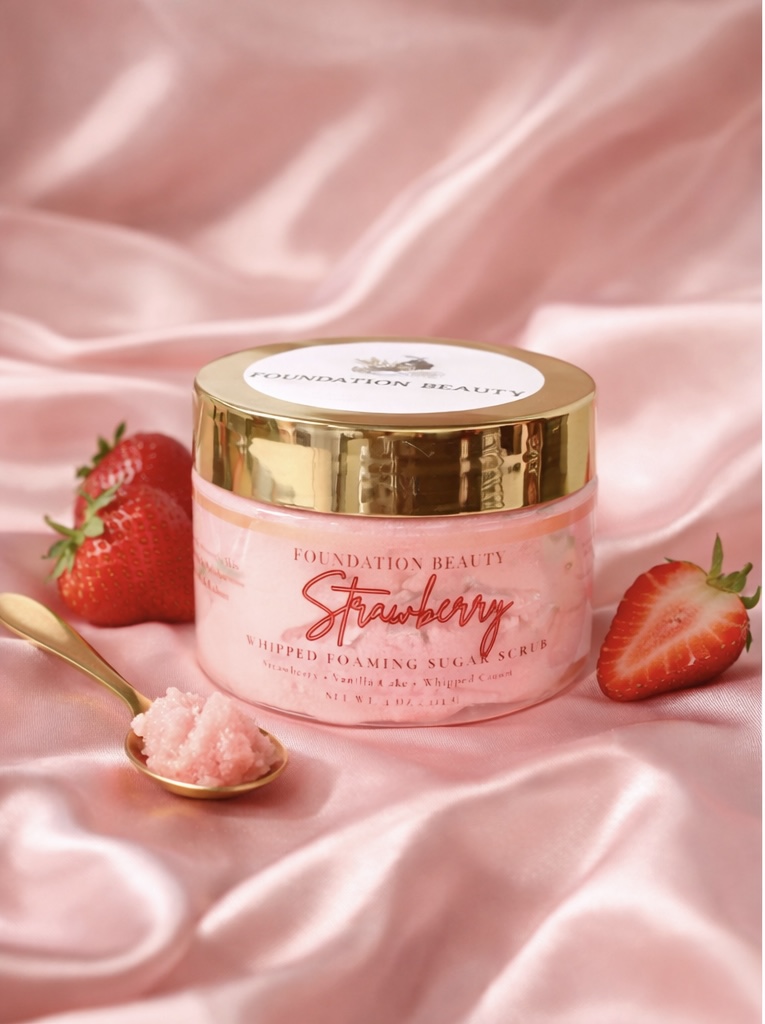 Pink jar of strawberry skincare cream with strawberries and a gold spoon on pink satin fabric.