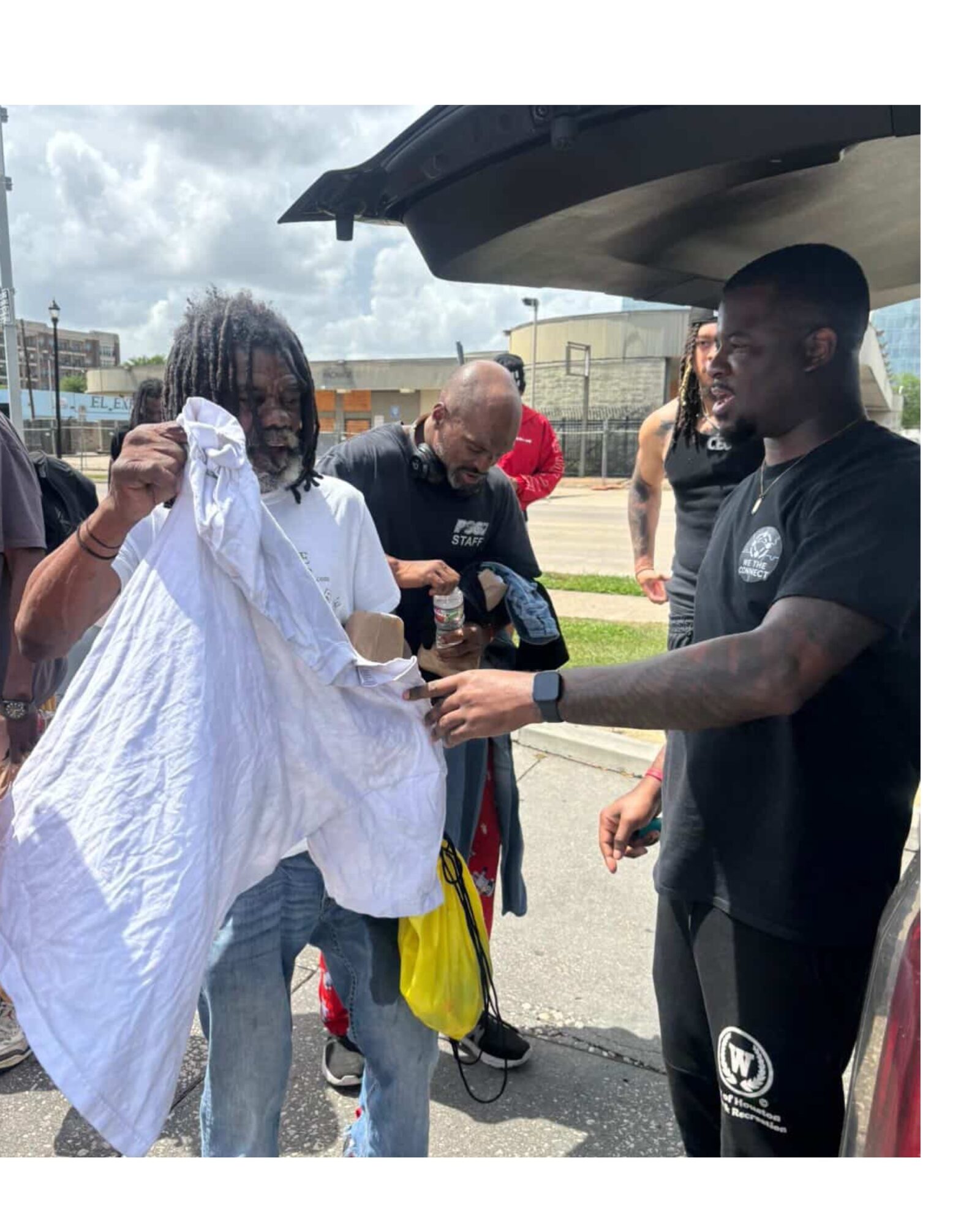 Group of people gathered outdoors near a vehicle, with one person holding a white cloth and others observing.