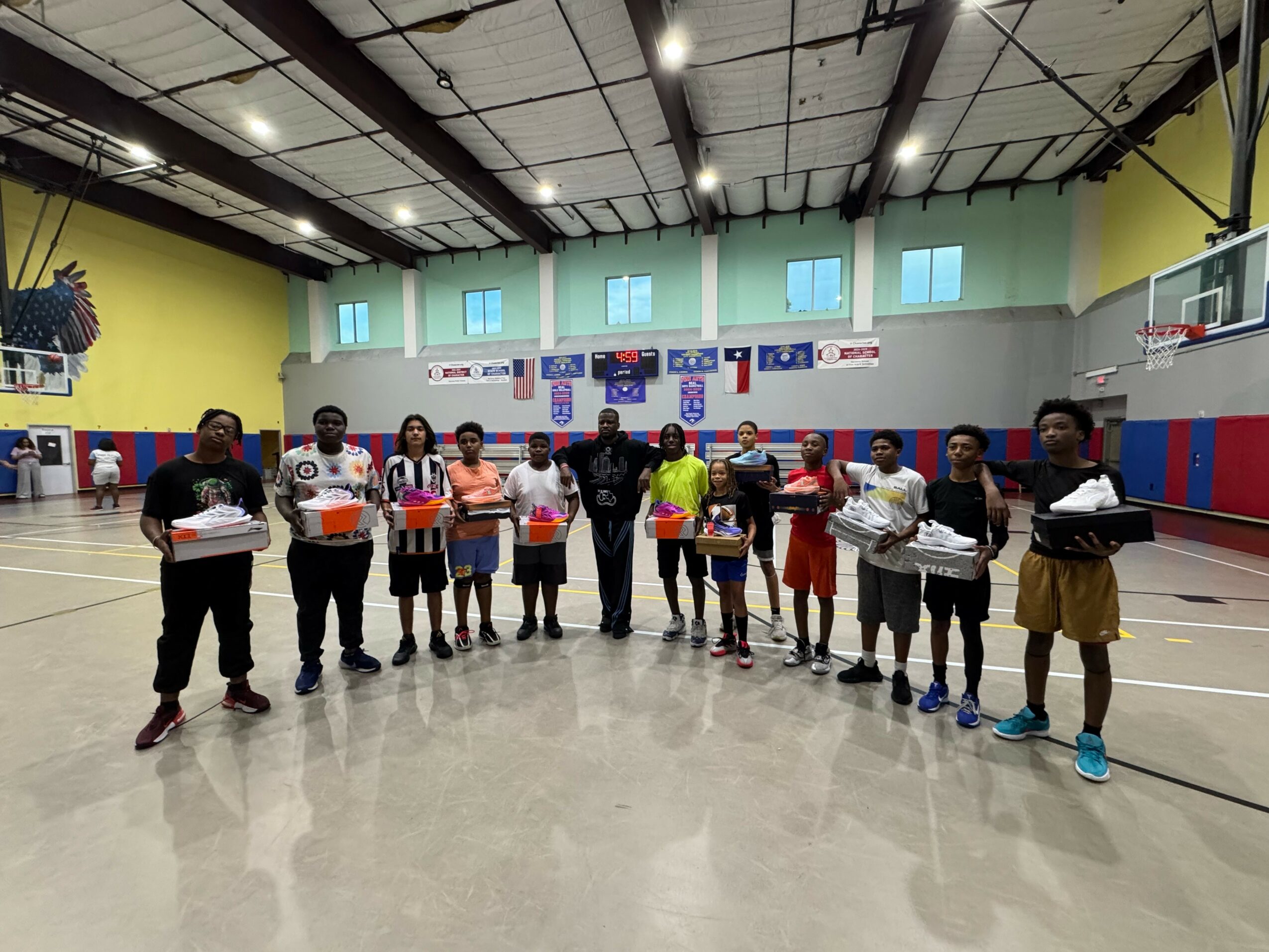 Group of children standing in a gymnasium holding boxes, with colorful walls and banners in the background.