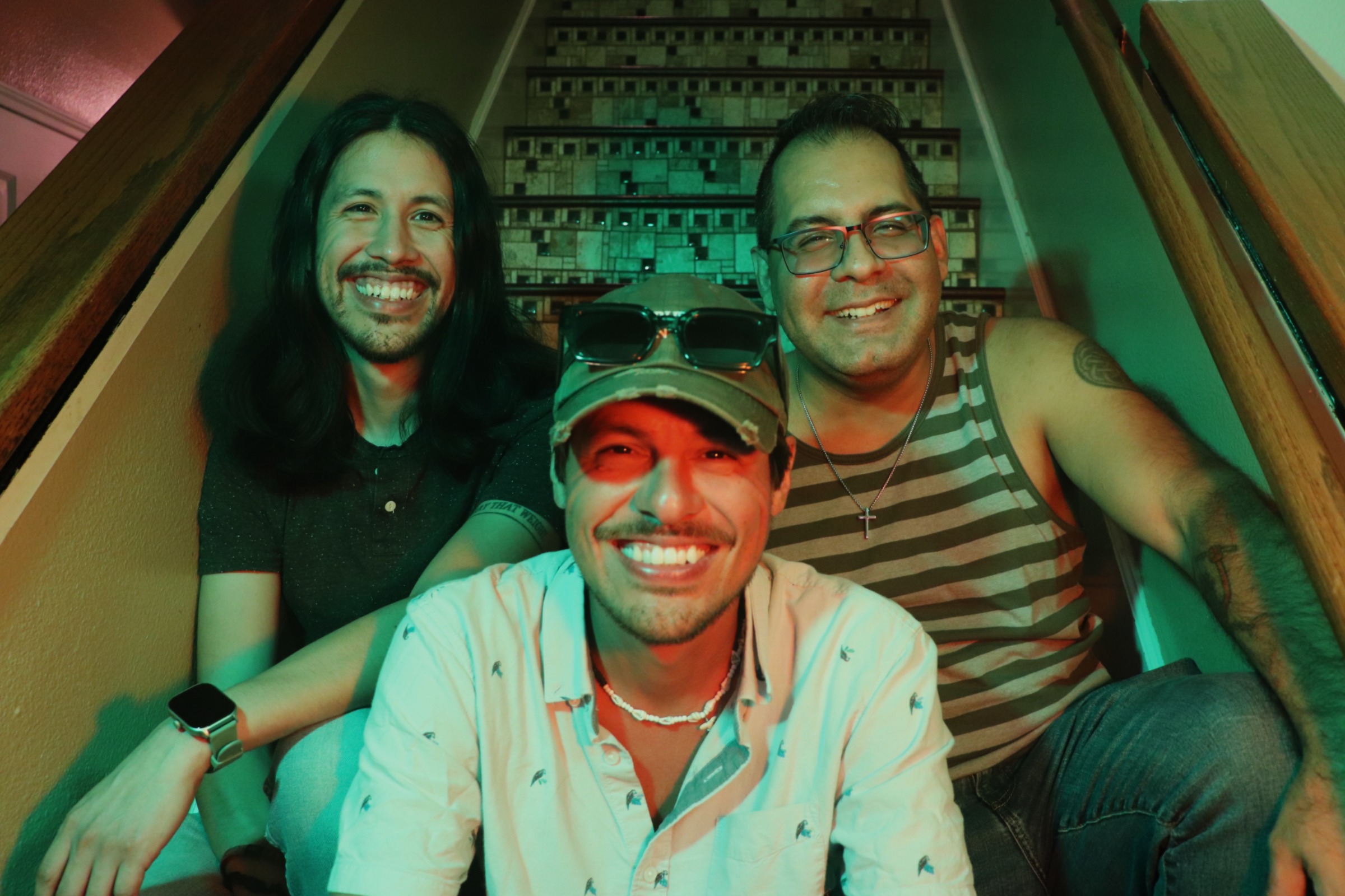 Three smiling people sitting on stairs, two women and one man, in casual clothing, with colorful lighting.