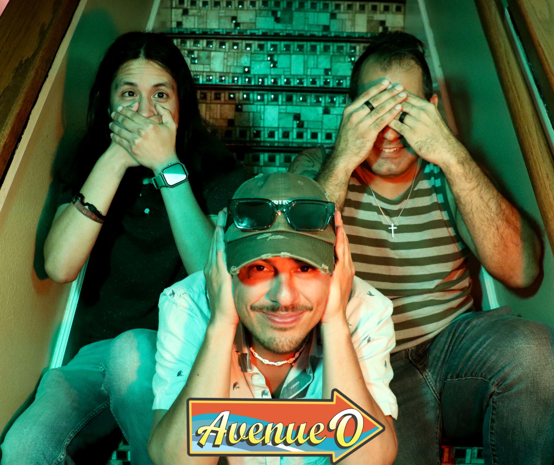 Three people sitting on stairs, covering their eyes or mouth, with a sign reading 'Avenue O' in front.