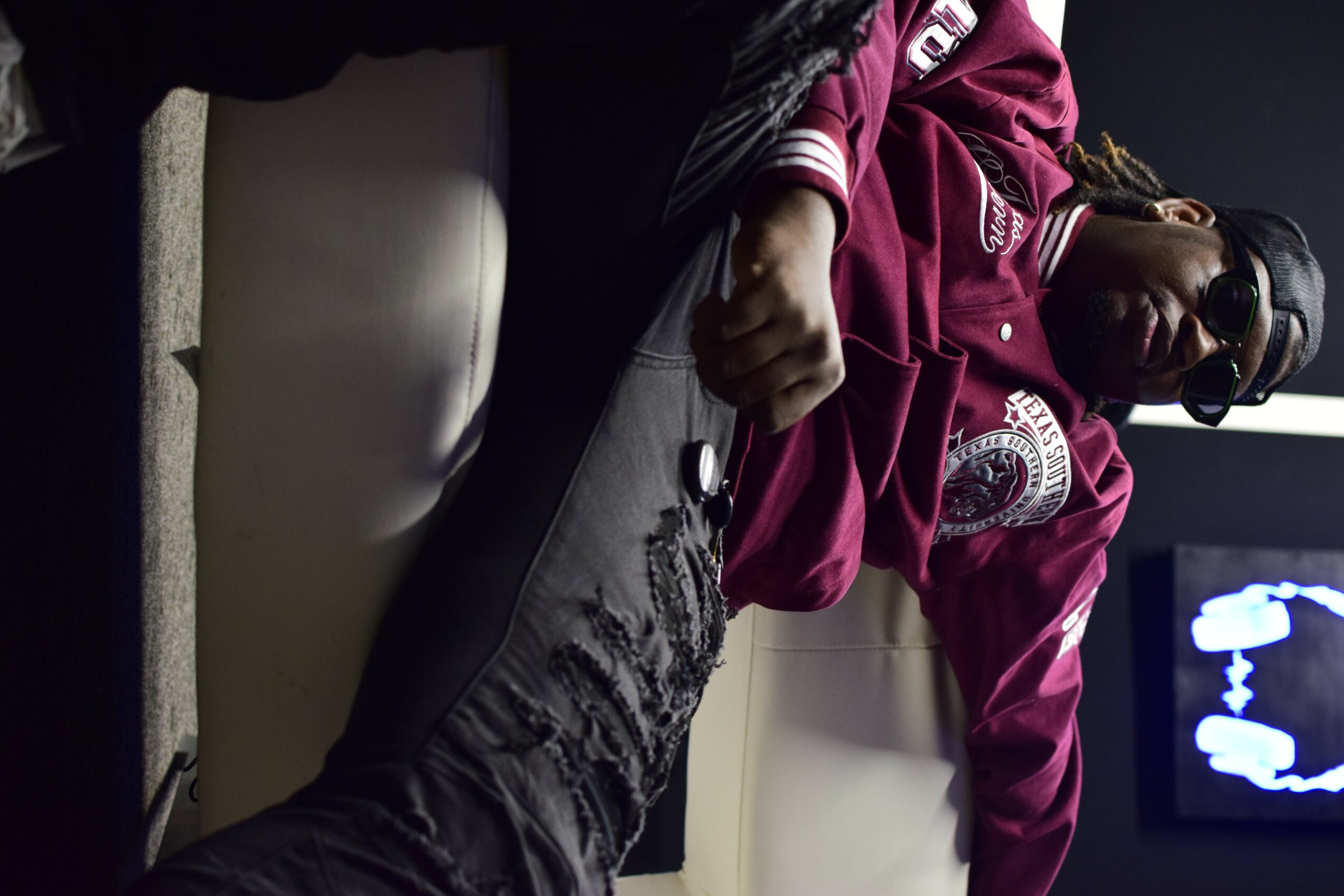 Person lying on a beige couch, wearing a maroon jacket and gray pants, with a TV screen in the background.