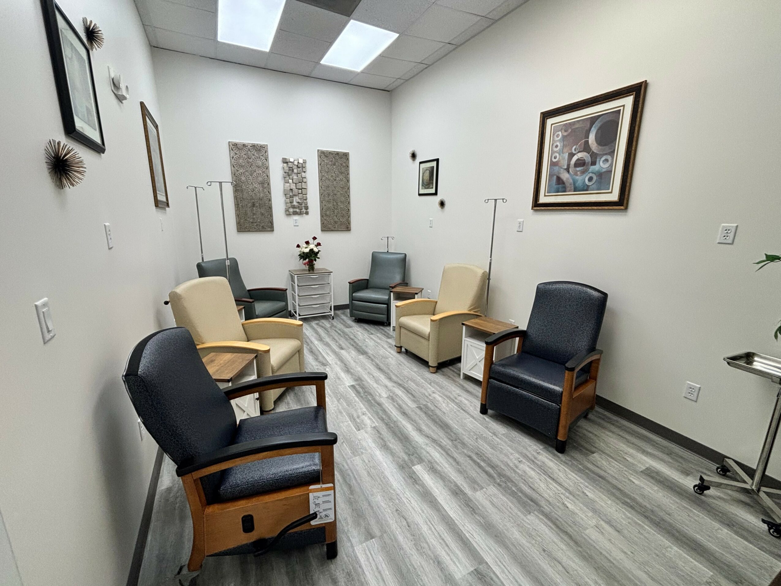 Waiting room with chairs, wall art, and a small table with flowers, in a well-lit space.