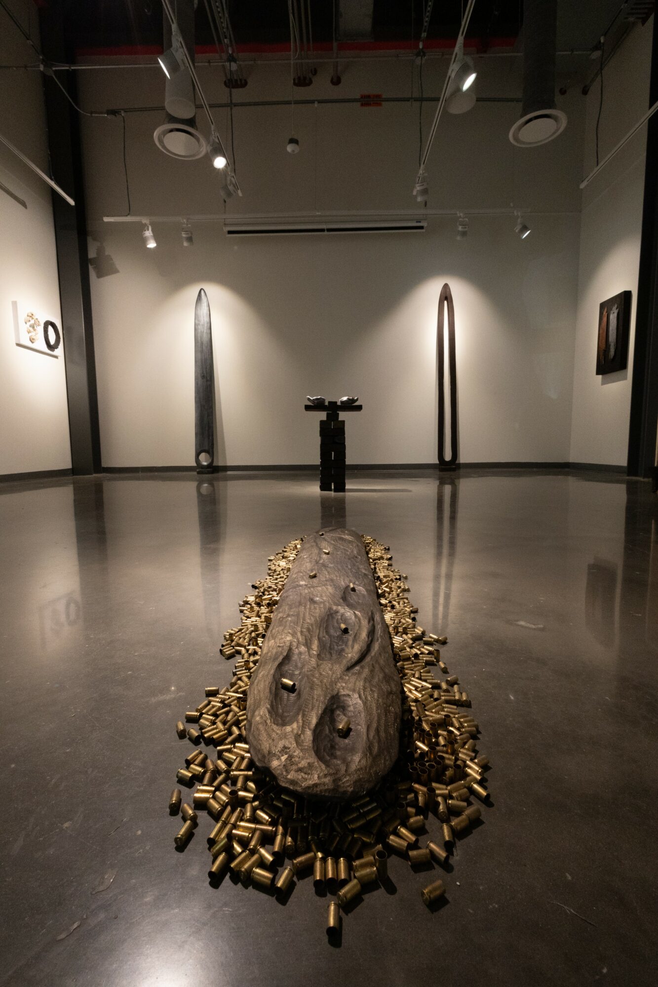 Art installation with a large, textured stone surrounded by numerous padlocks on a polished floor in a gallery.