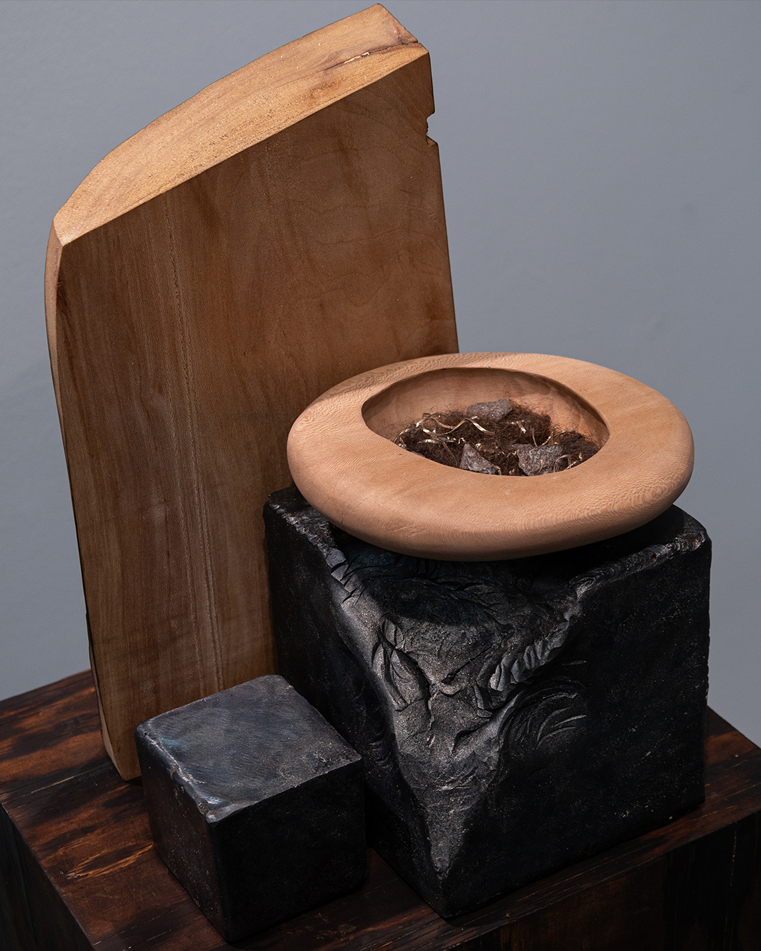 Wooden and stone sculpture with a bowl on top, displayed on a wooden surface against a plain background.