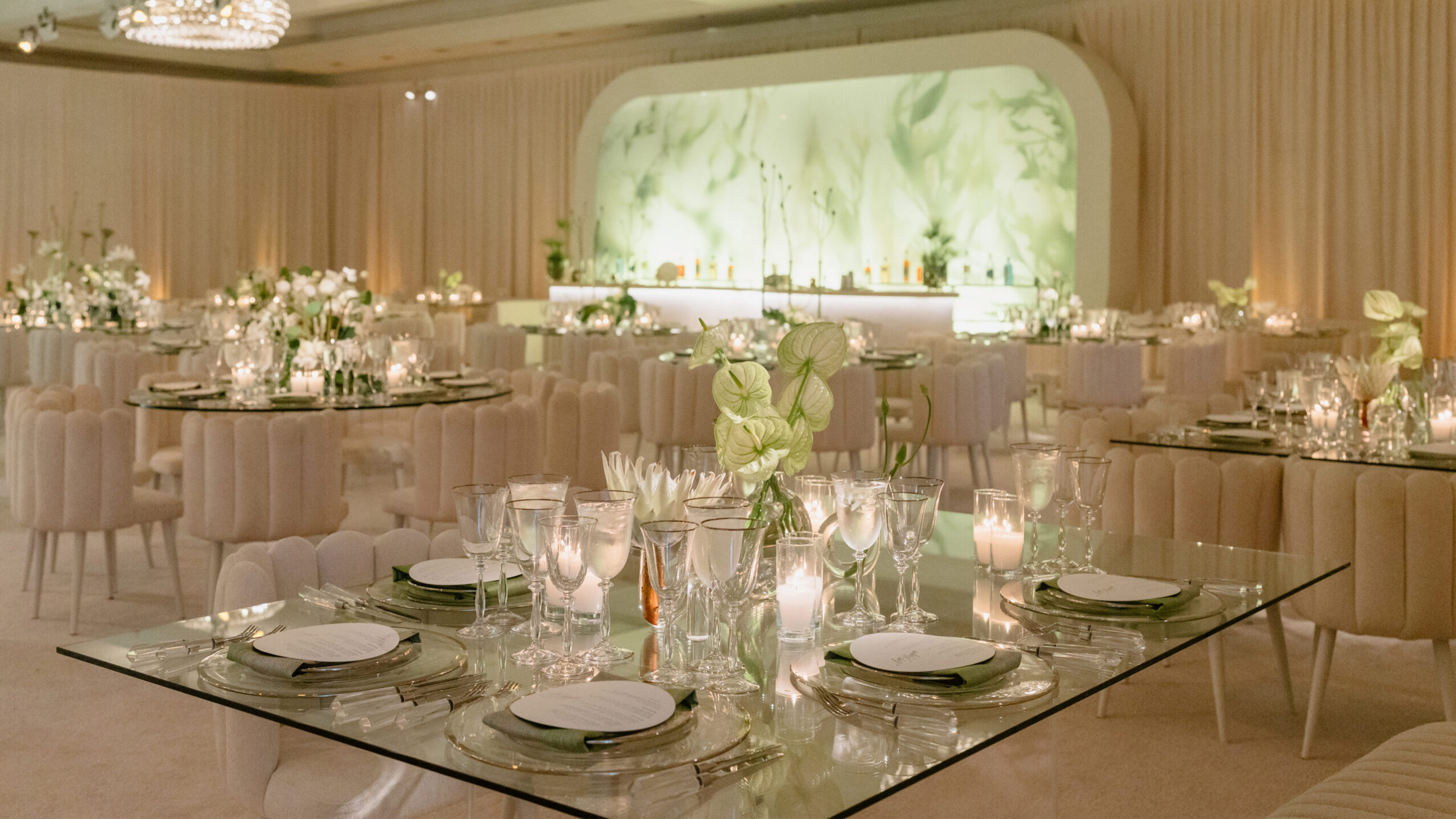Elegant banquet hall with round tables, floral centerpieces, and a large green marble backdrop.