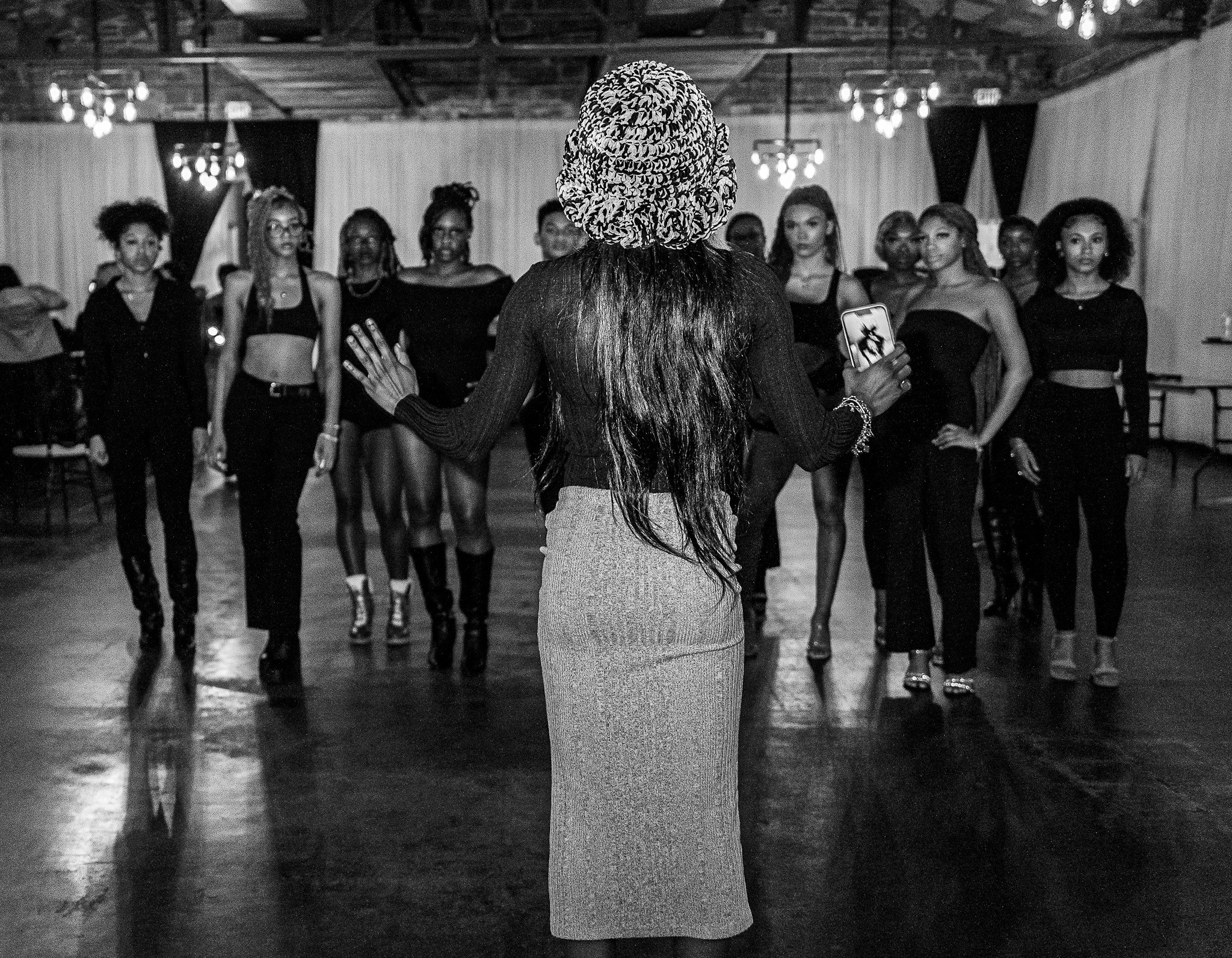 A woman with long hair and a patterned headscarf faces a group of women in a dance studio.