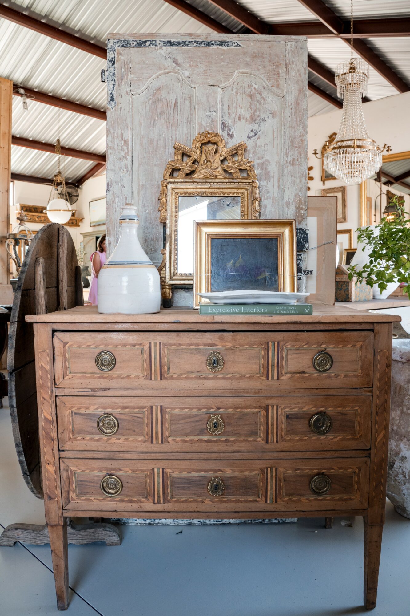 Wooden dresser with three rows of drawers, decorative items on top, and a mirror behind in a vintage store setting.