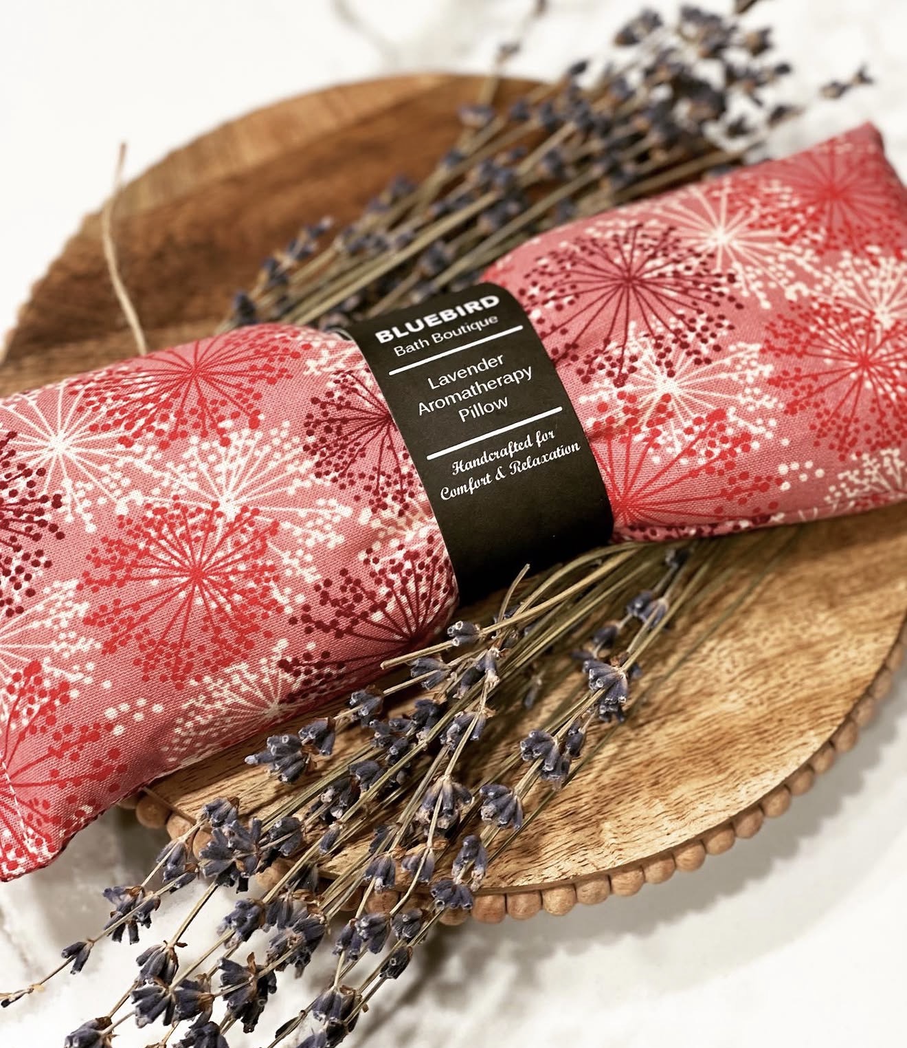 Two pink wrapped soap bars with white snowflake patterns on a wooden tray, surrounded by lavender sprigs.