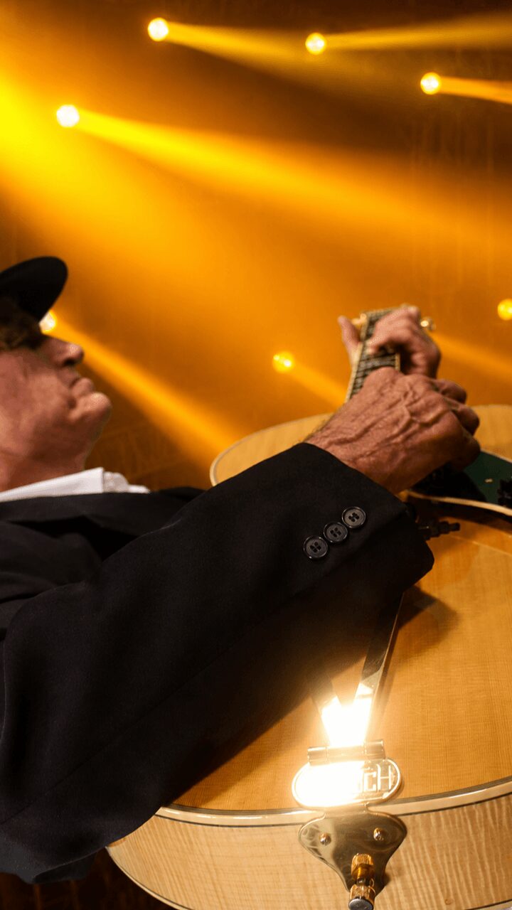 Person playing guitar on stage with yellow lighting in background
