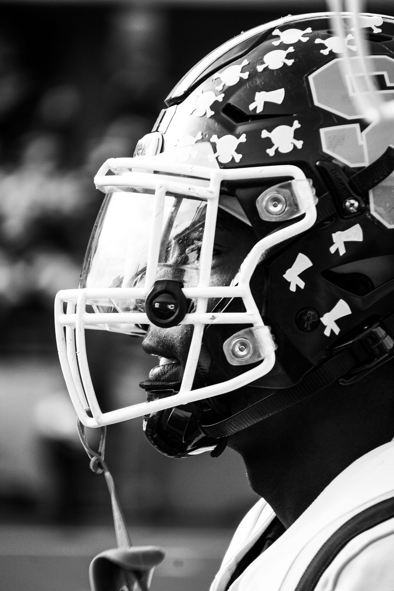 Close-up of a football helmet with faceguard, decorated with bone-shaped stickers, worn by a player on the field.