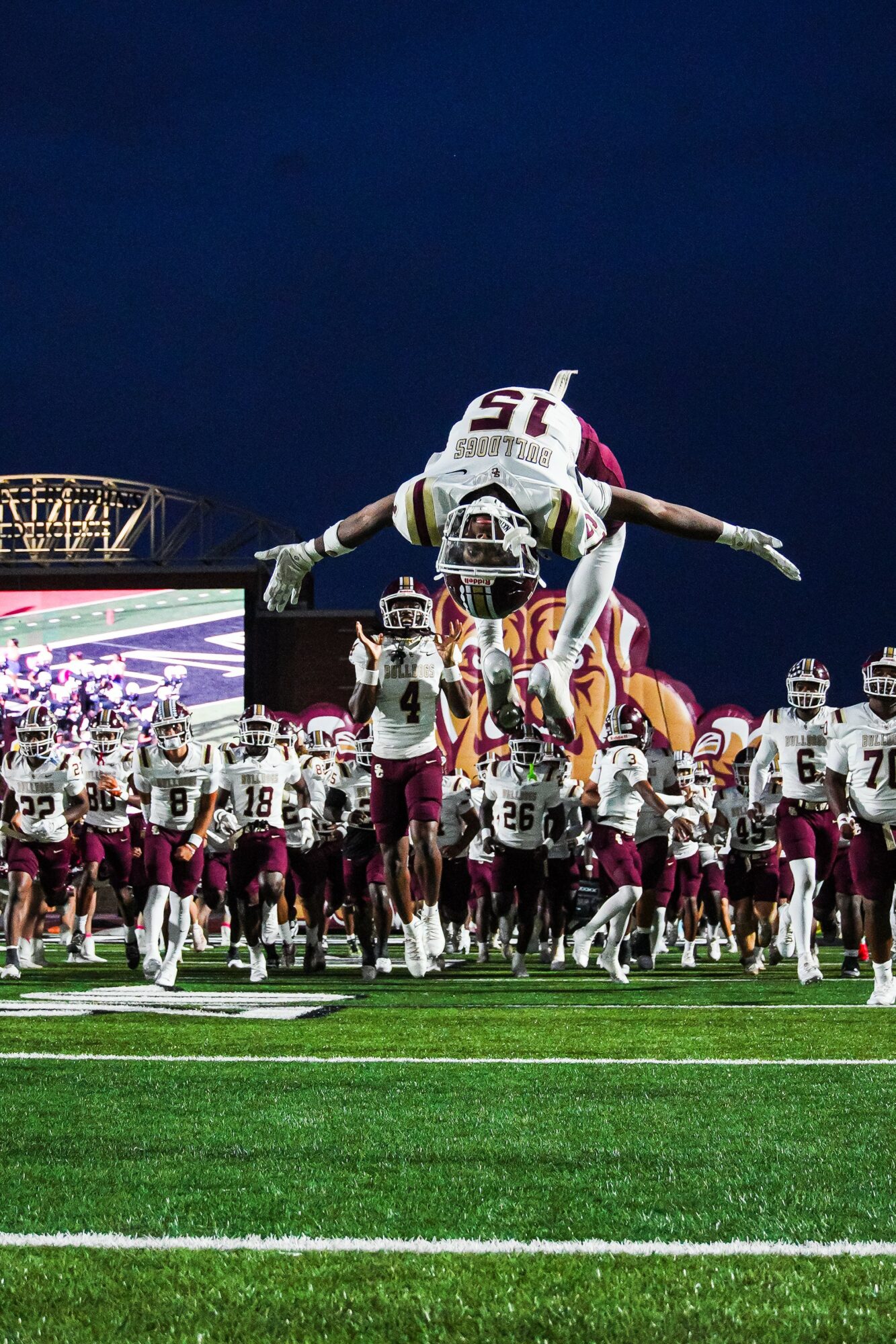 Football player mid-air during a game, surrounded by teammates on the field at night.