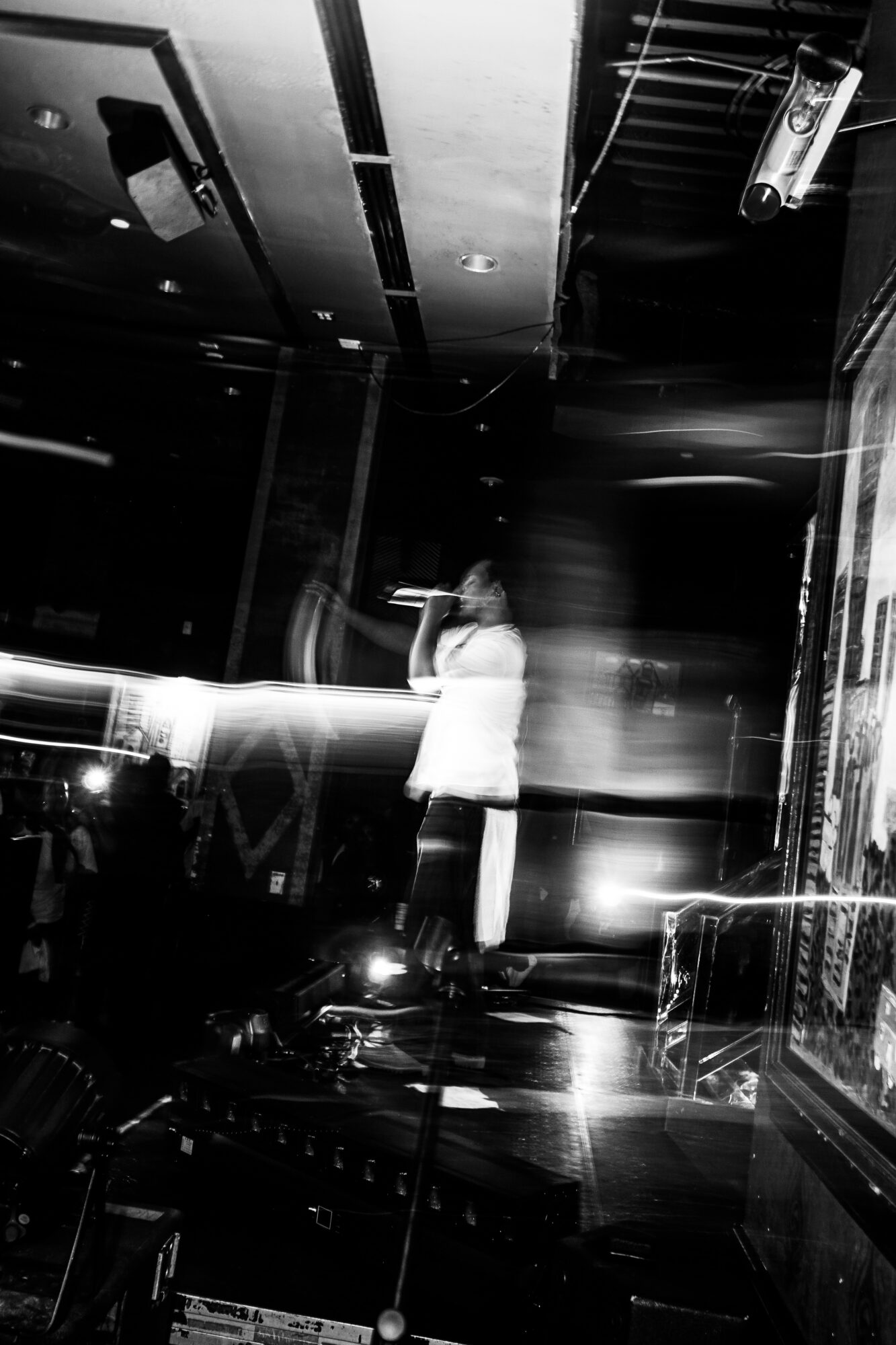 Person standing and speaking into a microphone on stage in a dark indoor setting.