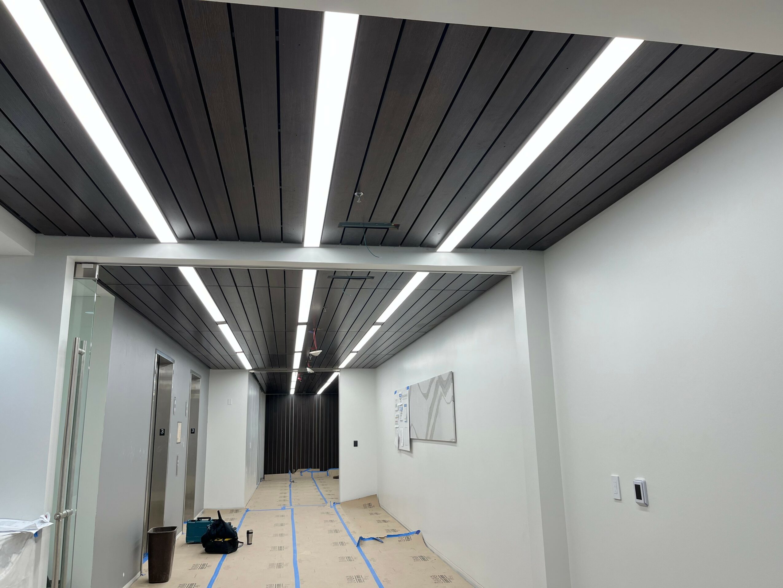 Ceiling with black panels and white light strips, white walls, hallway with doors, and a whiteboard on the wall.