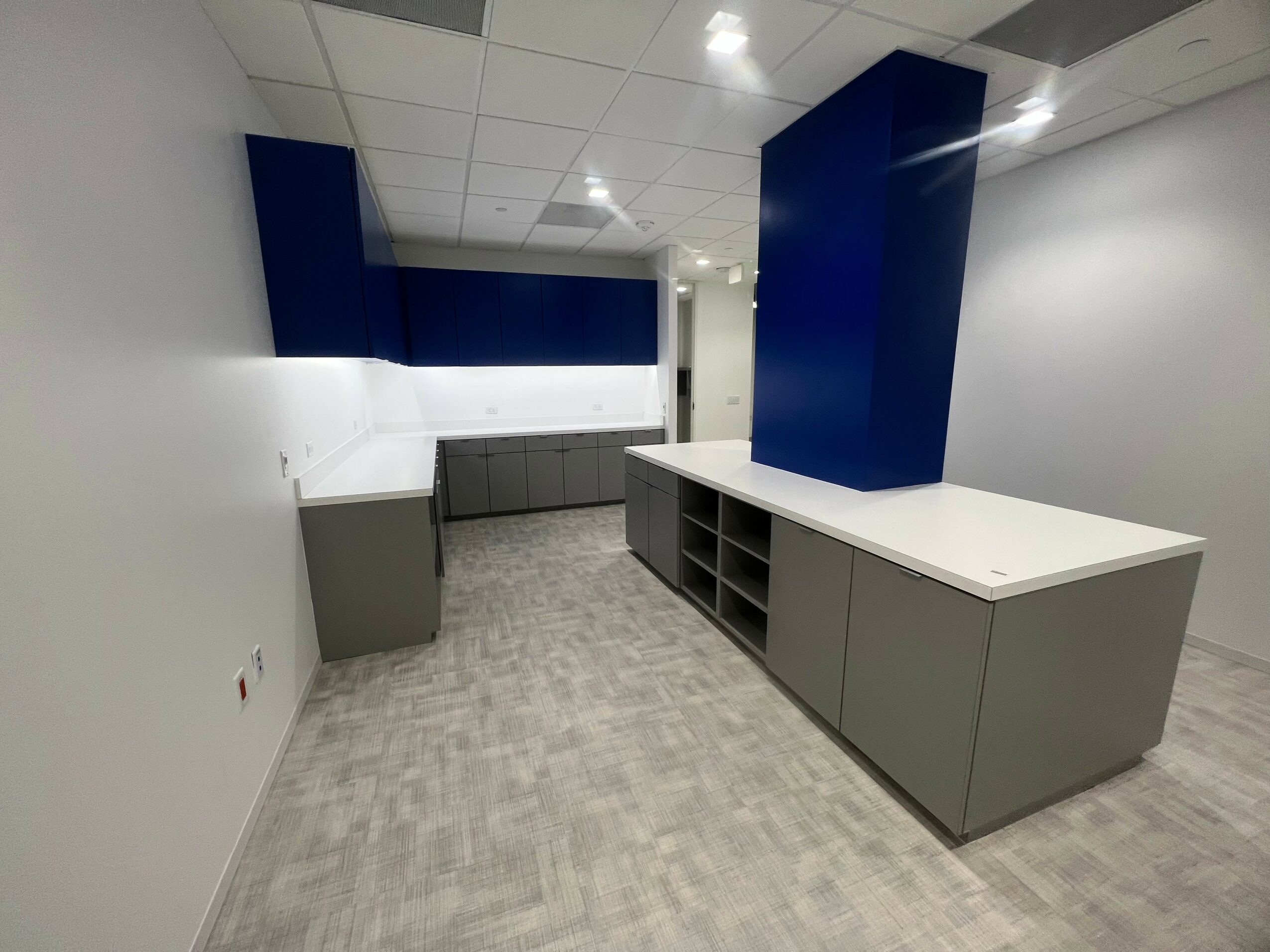Empty room with white walls, gray cabinets, and blue columns, featuring a gray floor and ceiling lights.