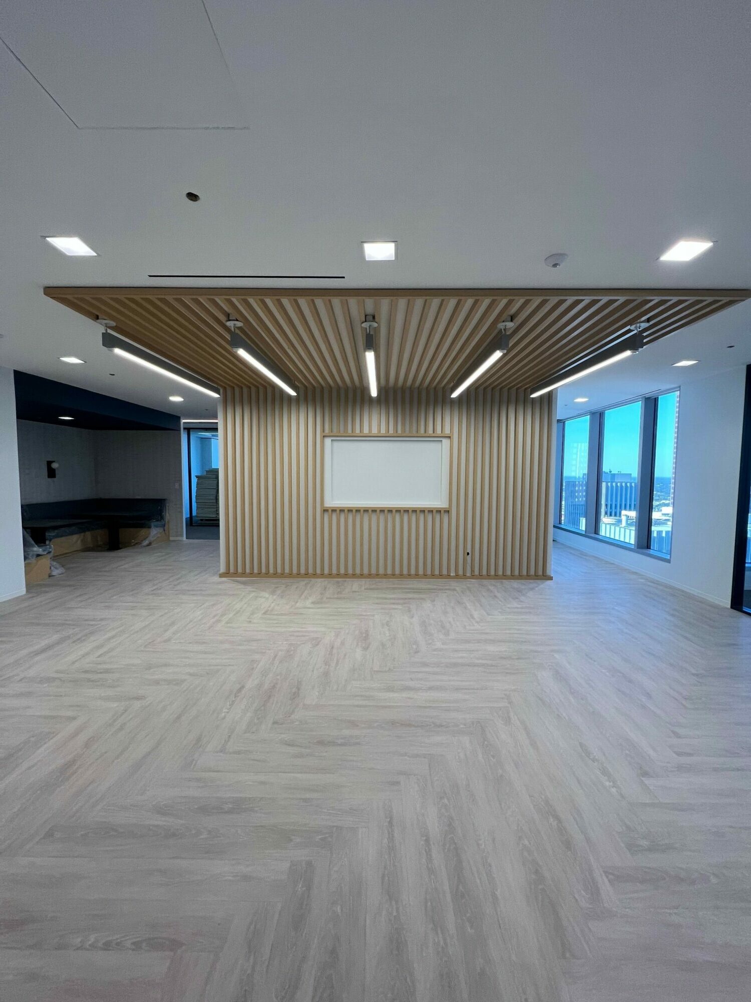 Empty room with wooden wall, large window, and light-colored floor, ceiling with lights, and a mirror on the wall.