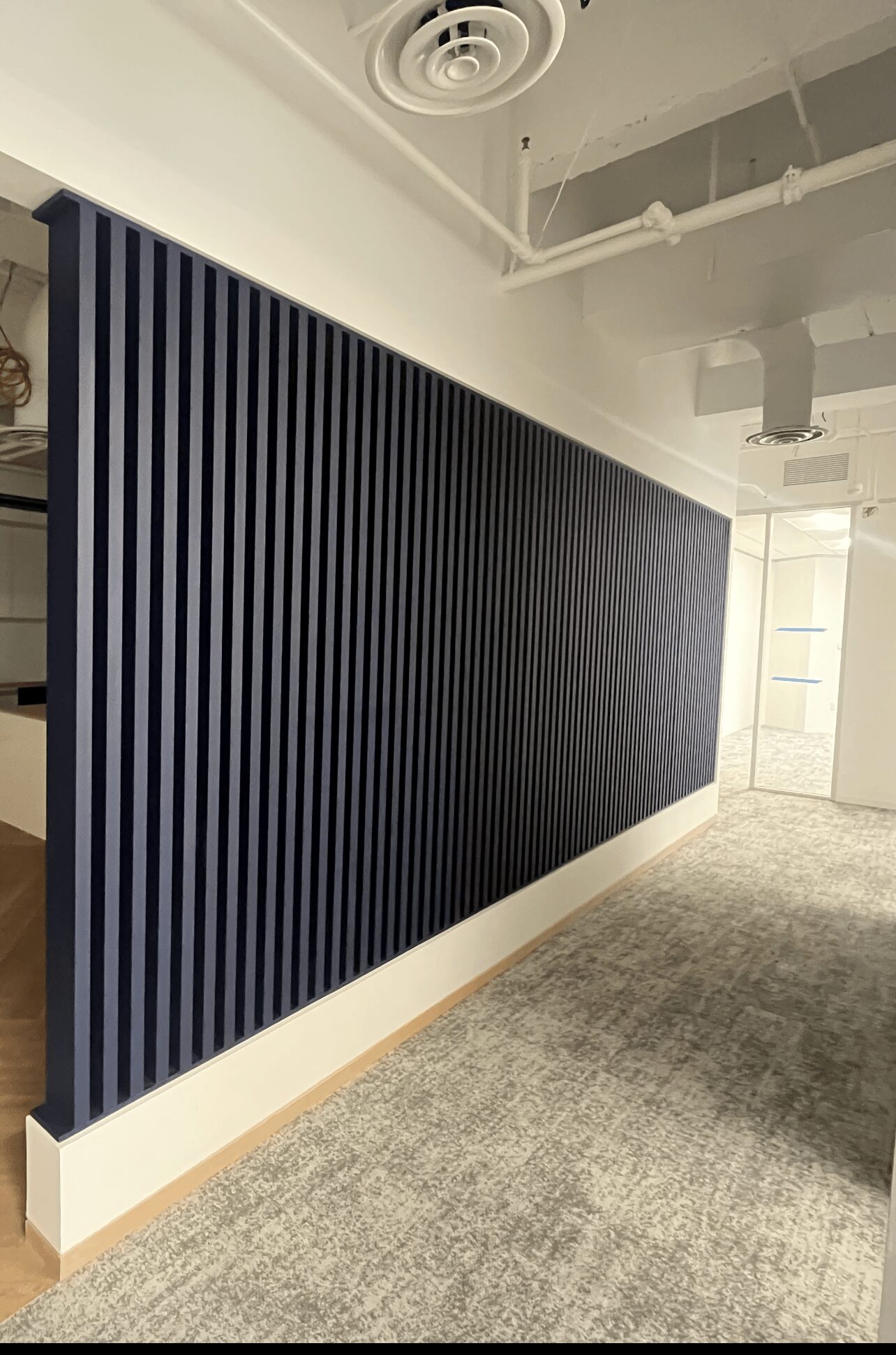 Interior space with a dark blue vertical slat wall, ceiling vent, and light-colored carpeted floor.