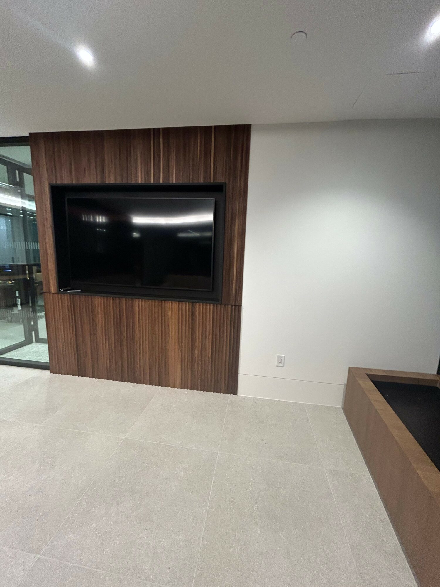 Living room with a wall-mounted TV on a wooden panel, white wall, and light-colored floor.