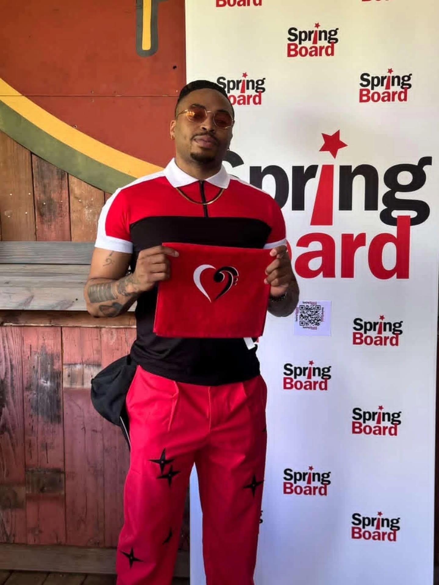 Man holding a red cloth with a heart symbol, standing in front of a Spring Board backdrop, wearing red and black clothing.
