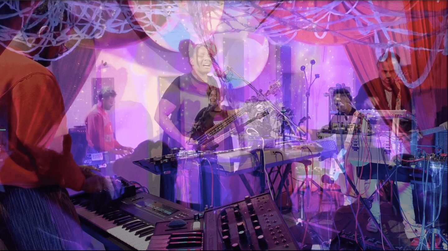 Band performing on stage with multiple musicians playing instruments, colorful stage lighting, and decorative elements.