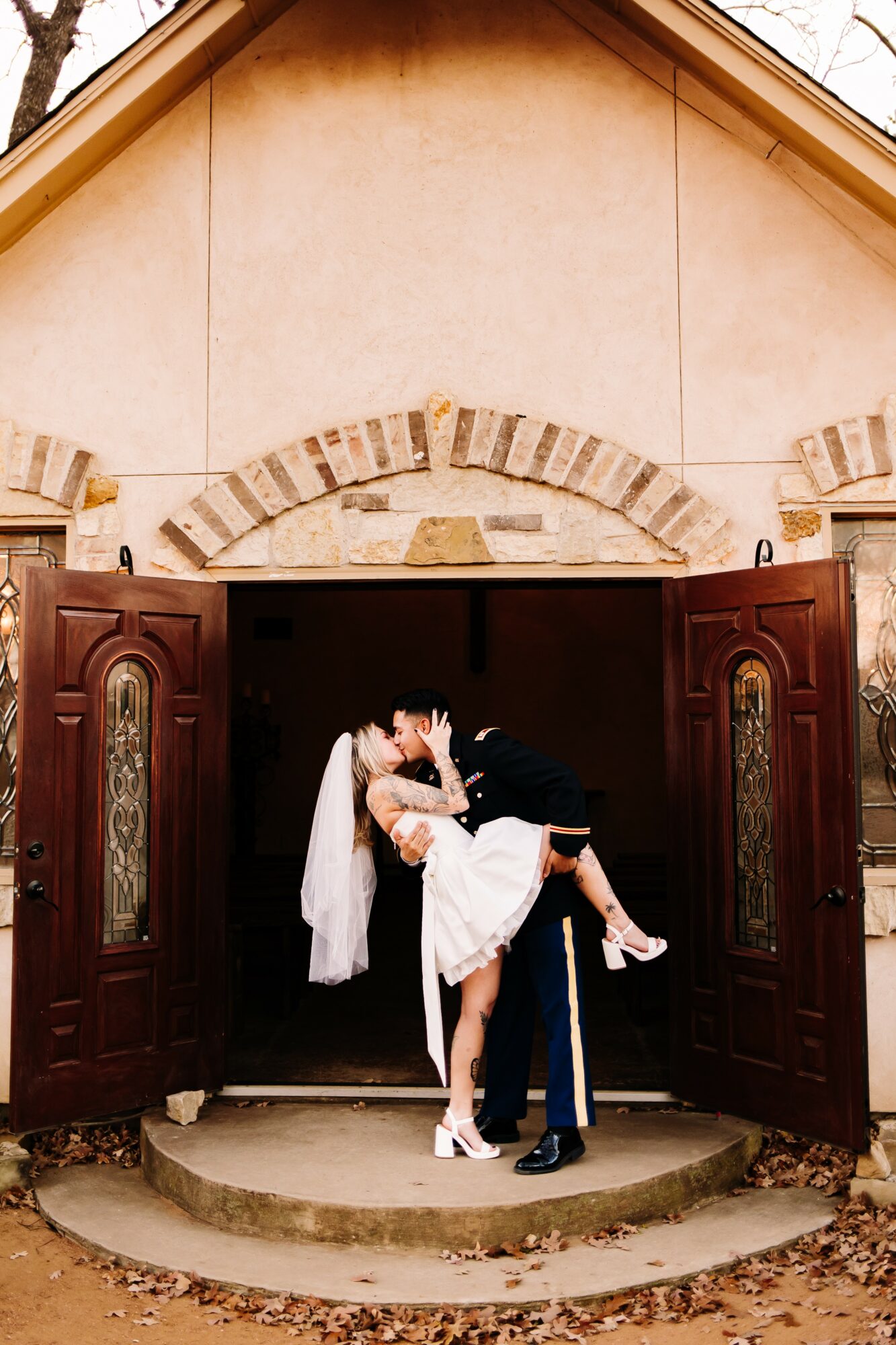 Couple dancing in front of open church doors, woman in white dress, man in dark suit, on stone steps.