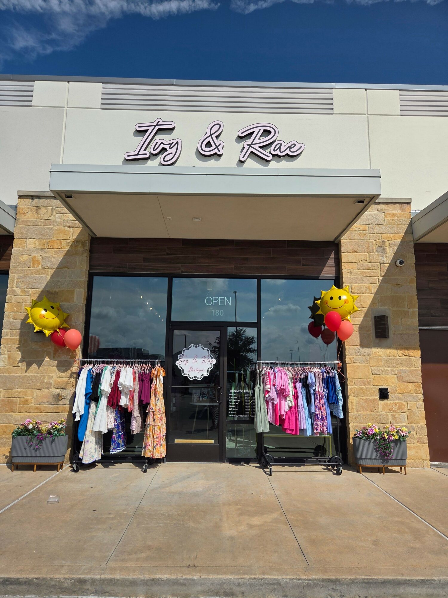 Storefront with clothing displays outside, yellow and red balloons, and a sign reading 'The Rise'.