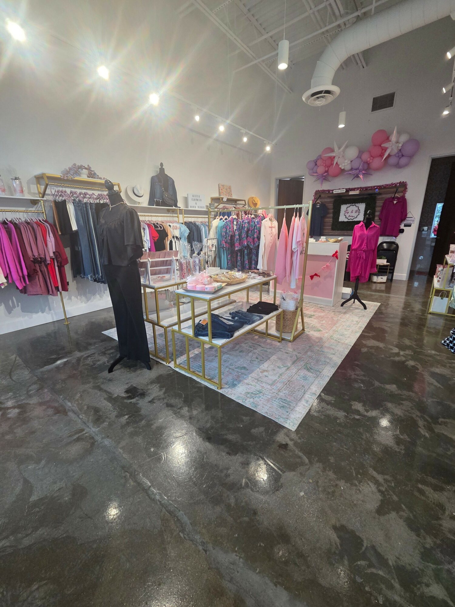 Clothing display with pink and purple garments in a store, with a person browsing nearby, and bright lighting.