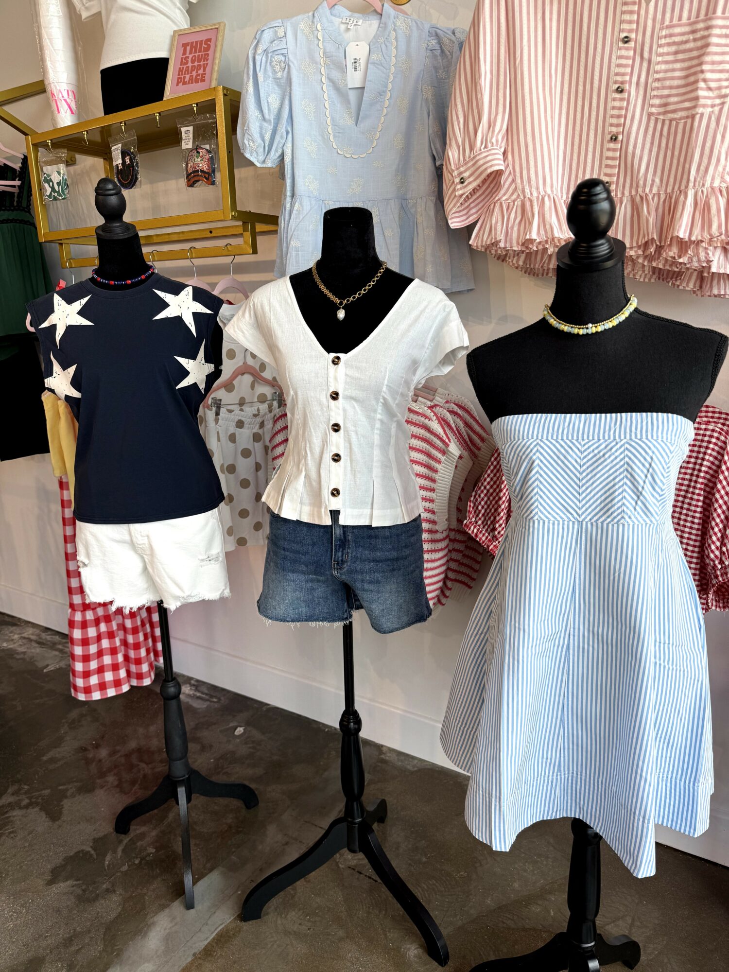 Display of three mannequins dressed in casual summer outfits, with clothing racks and a mirror in the background.