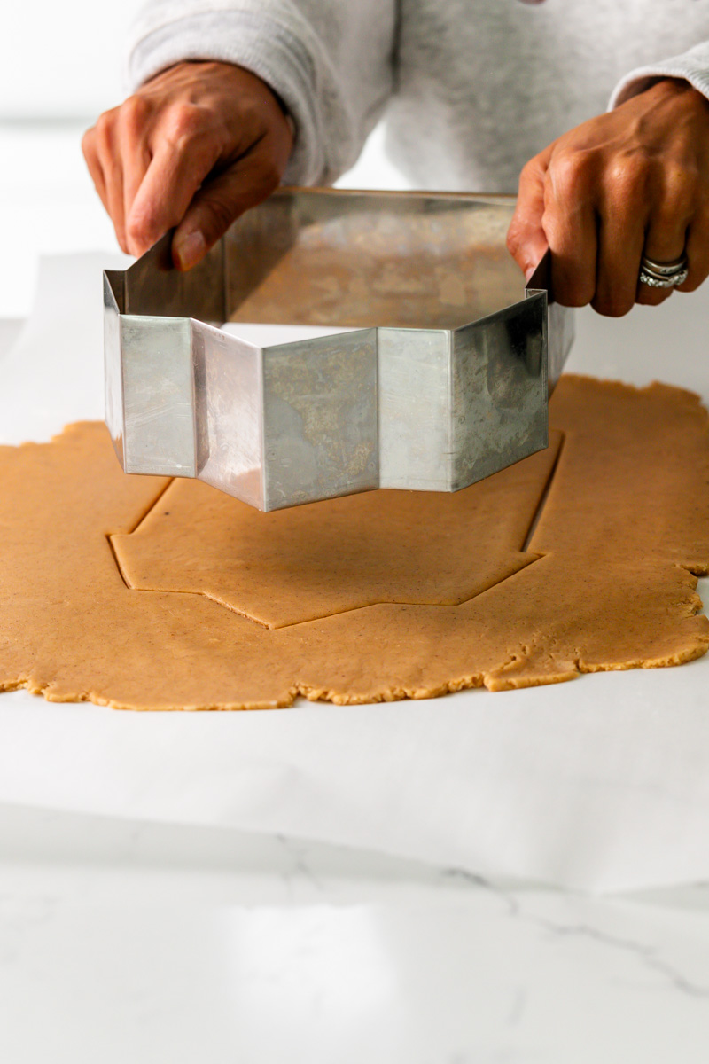 Person using a metal cookie cutter to cut dough on a white surface.
