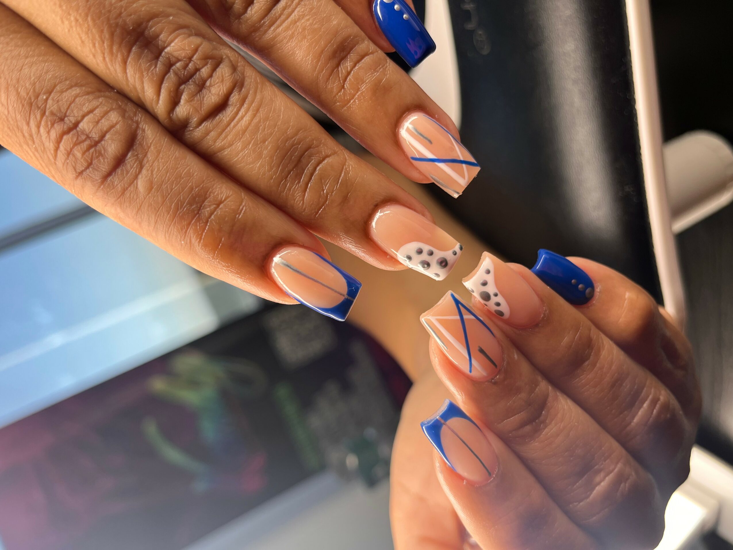 Close-up of hands with colorful, geometric nail art, including blue, beige, and dotted designs, on well-manicured nails.