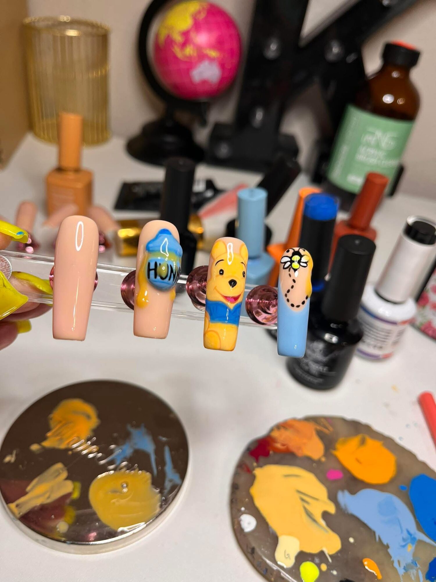 Nail polish bottles and tools arranged on a surface with paint palettes in the foreground.
