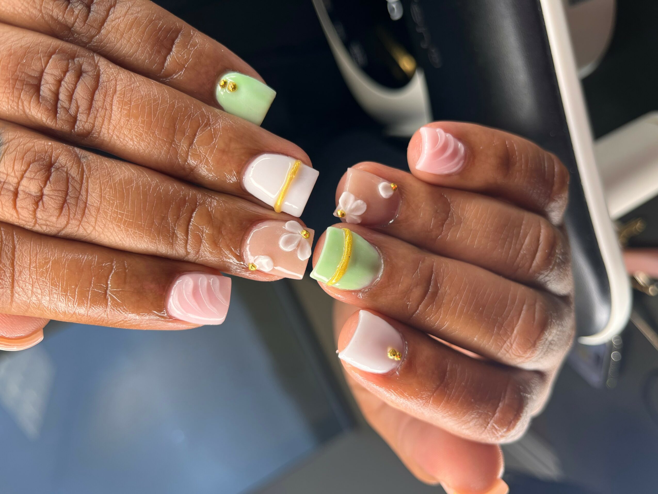 Close-up of hands with colorful, decorated nails resting on a car steering wheel.