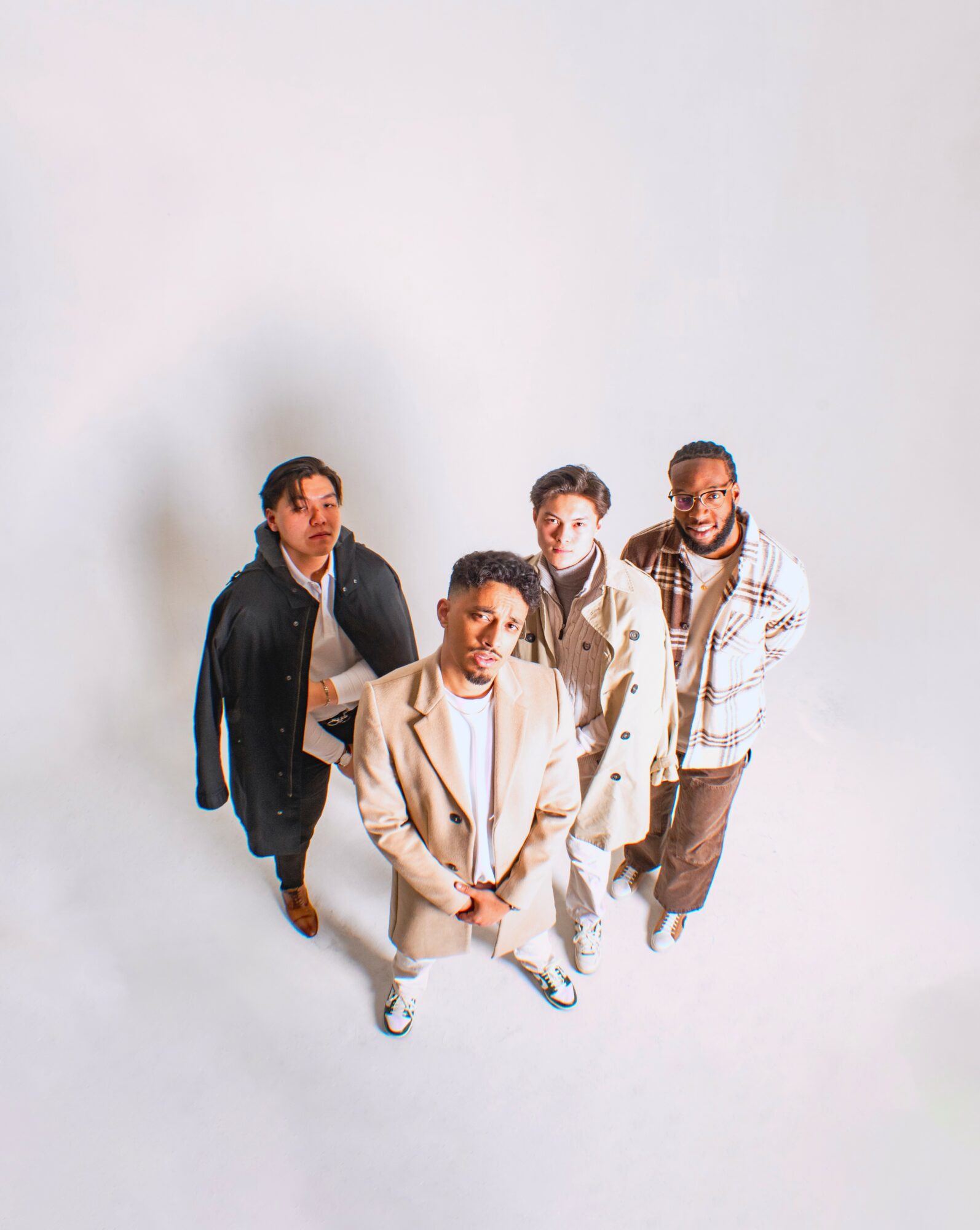 Four people standing together, smiling, in a studio with a plain white background.