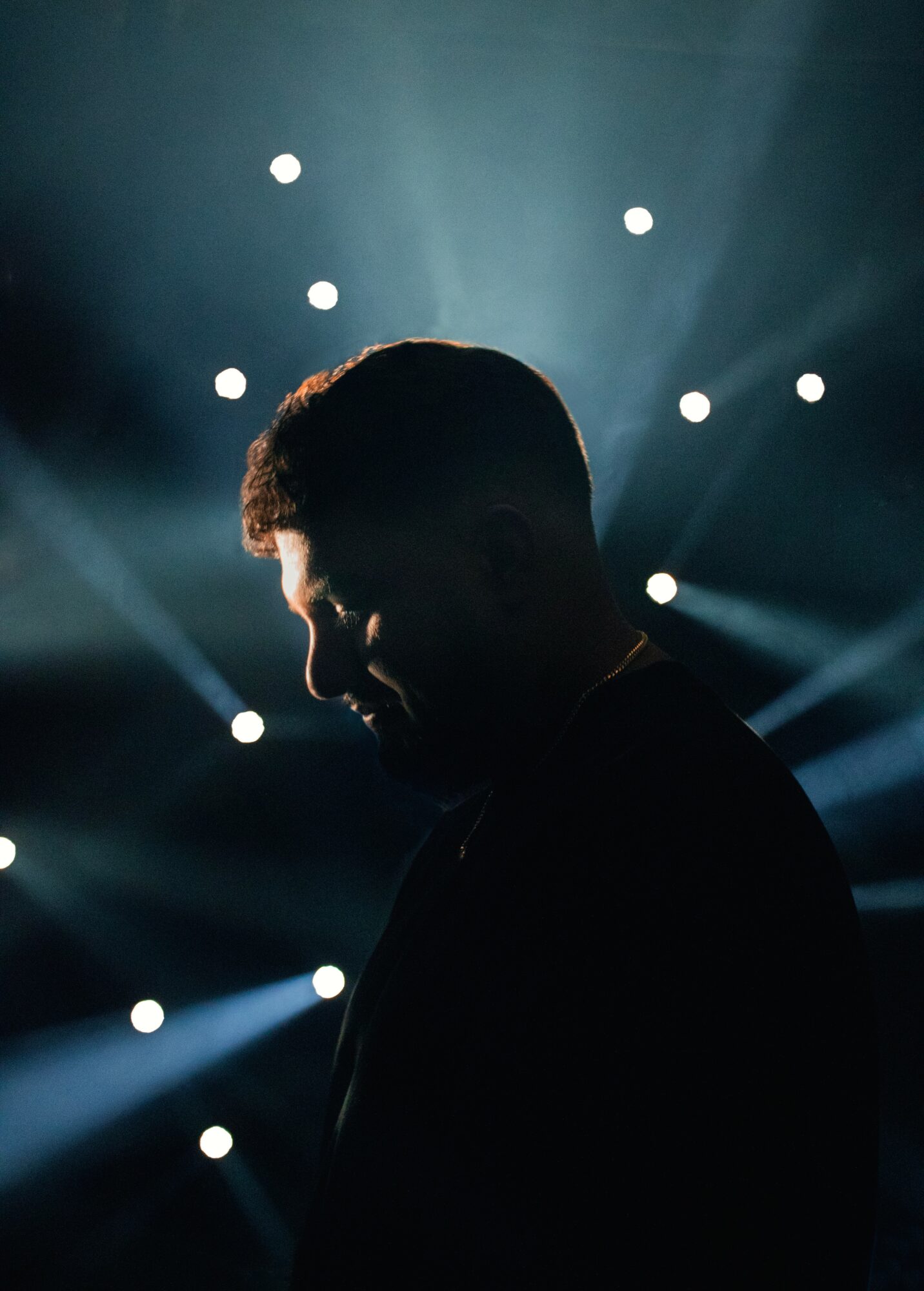 Silhouette of a person with a background of bright lights and rays, facing downward, in a dark setting.