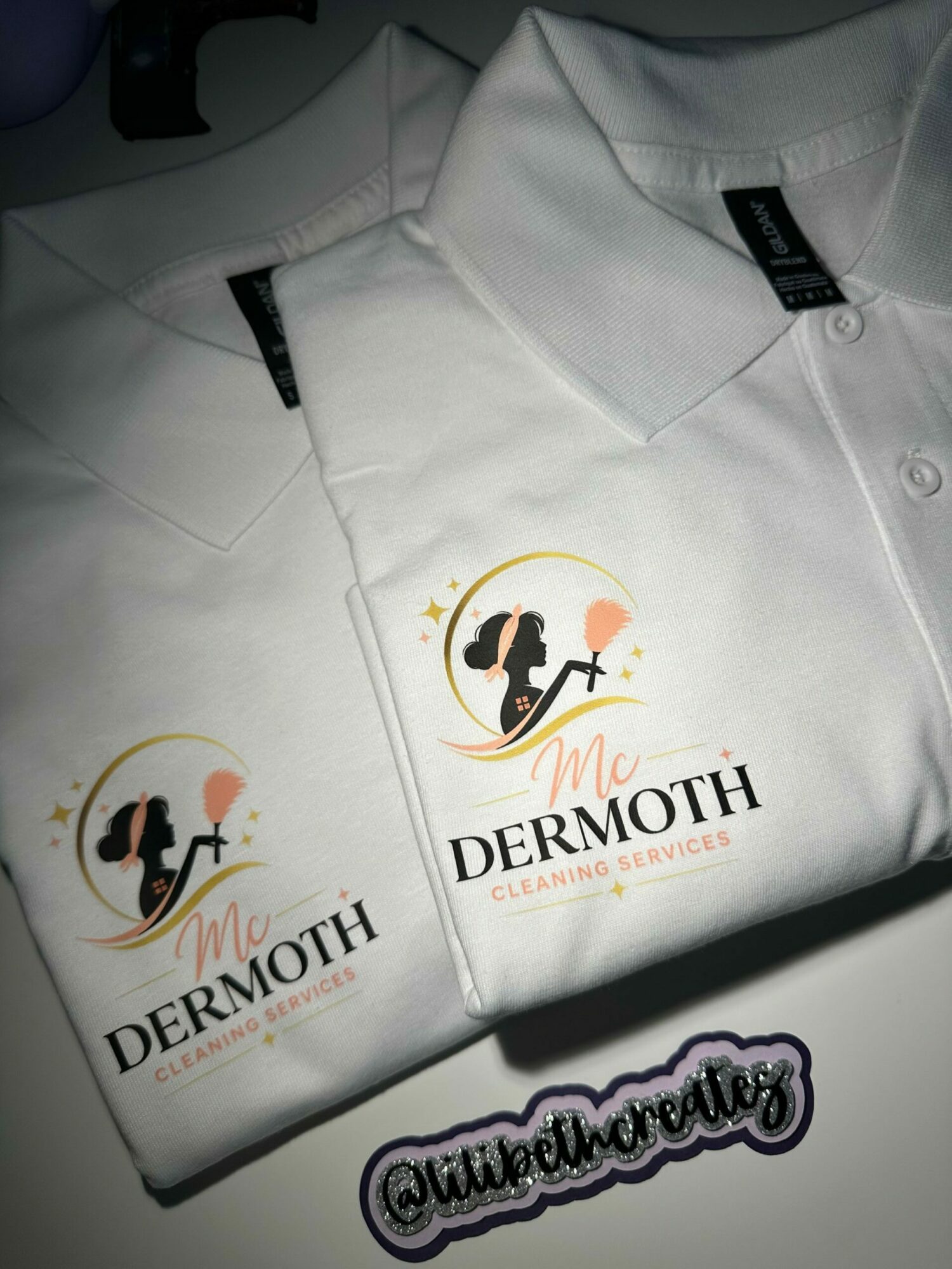 Two white uniforms with Dermmooth logos, one with a black tag, displayed on a surface.
