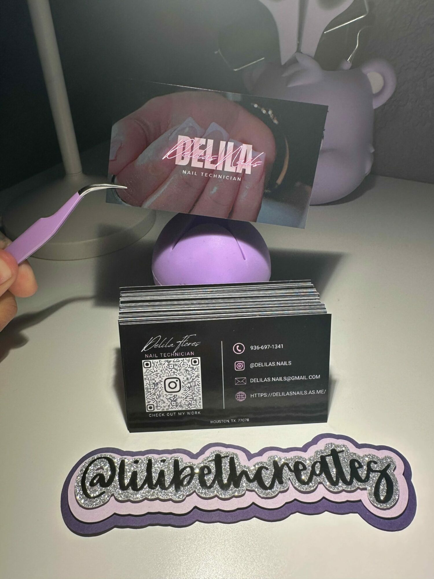 Desk with purple speaker, business card, and social media sticker, viewed from above. Person's hand holding a purple and white object.