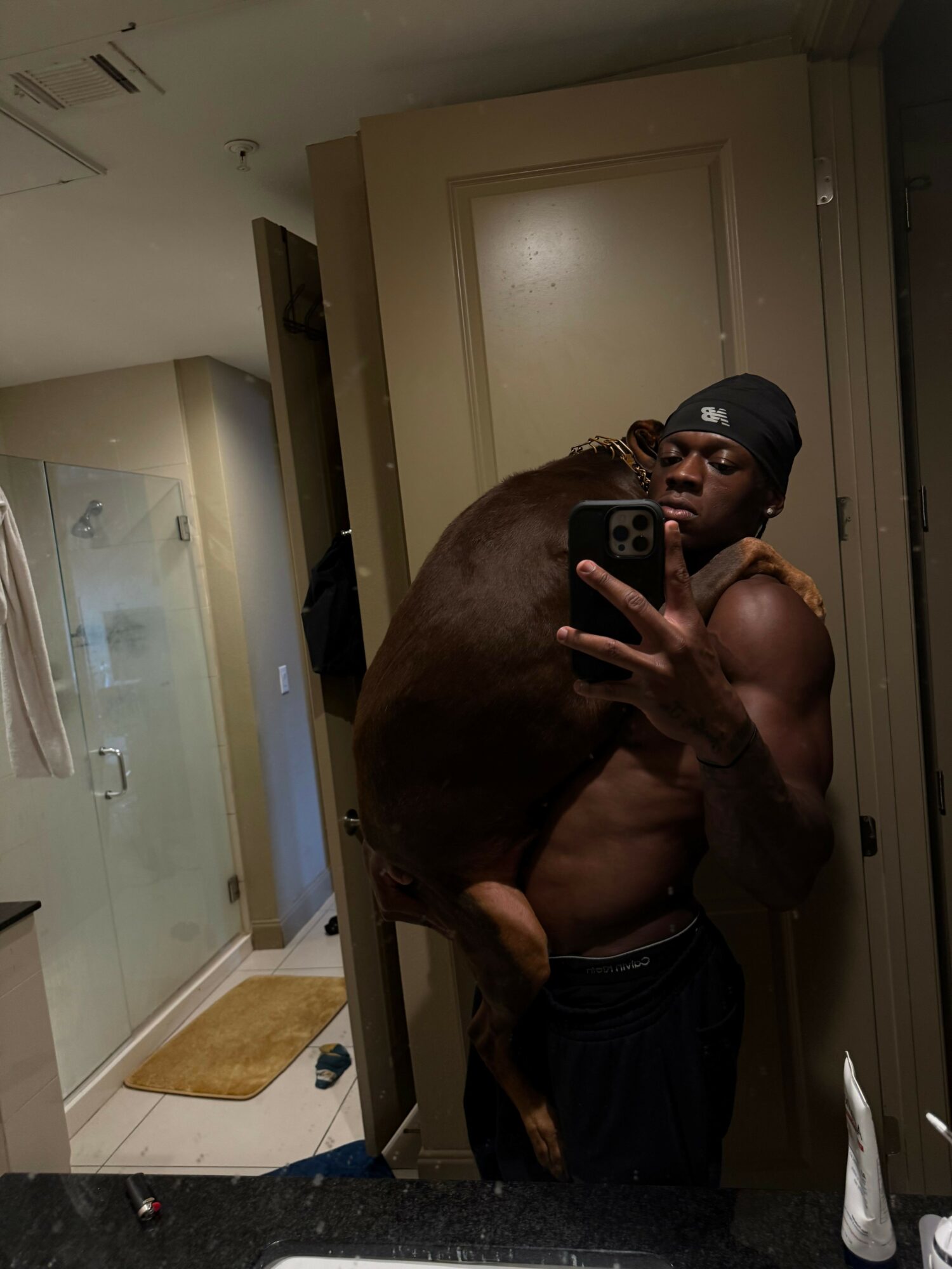 Person taking a mirror selfie with a dog, both reflected in a mirror, in a room with a door and hallway visible.