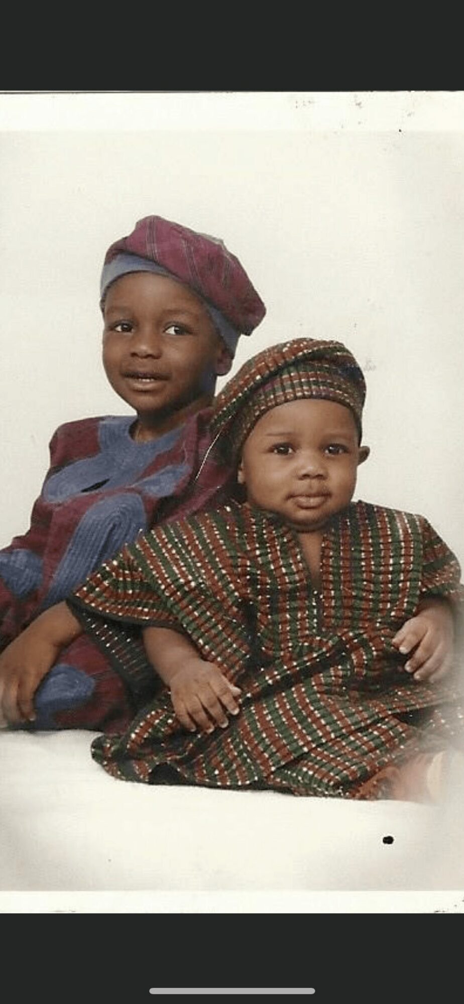 Two children sitting together, one older girl and a younger girl, both wearing traditional clothing and head coverings.