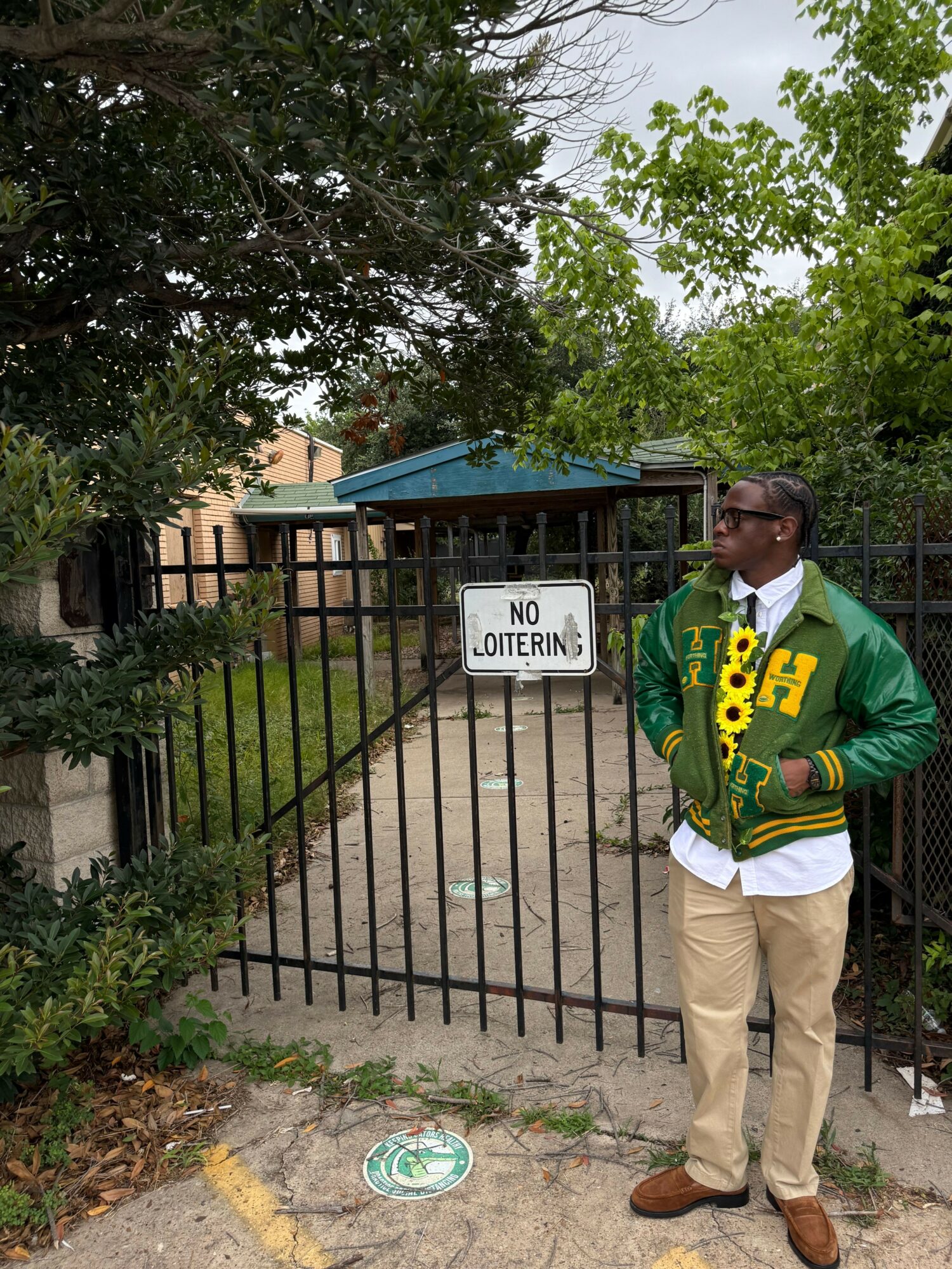 Person standing next to a black gate with a no trespassing sign, trees and a building in background.