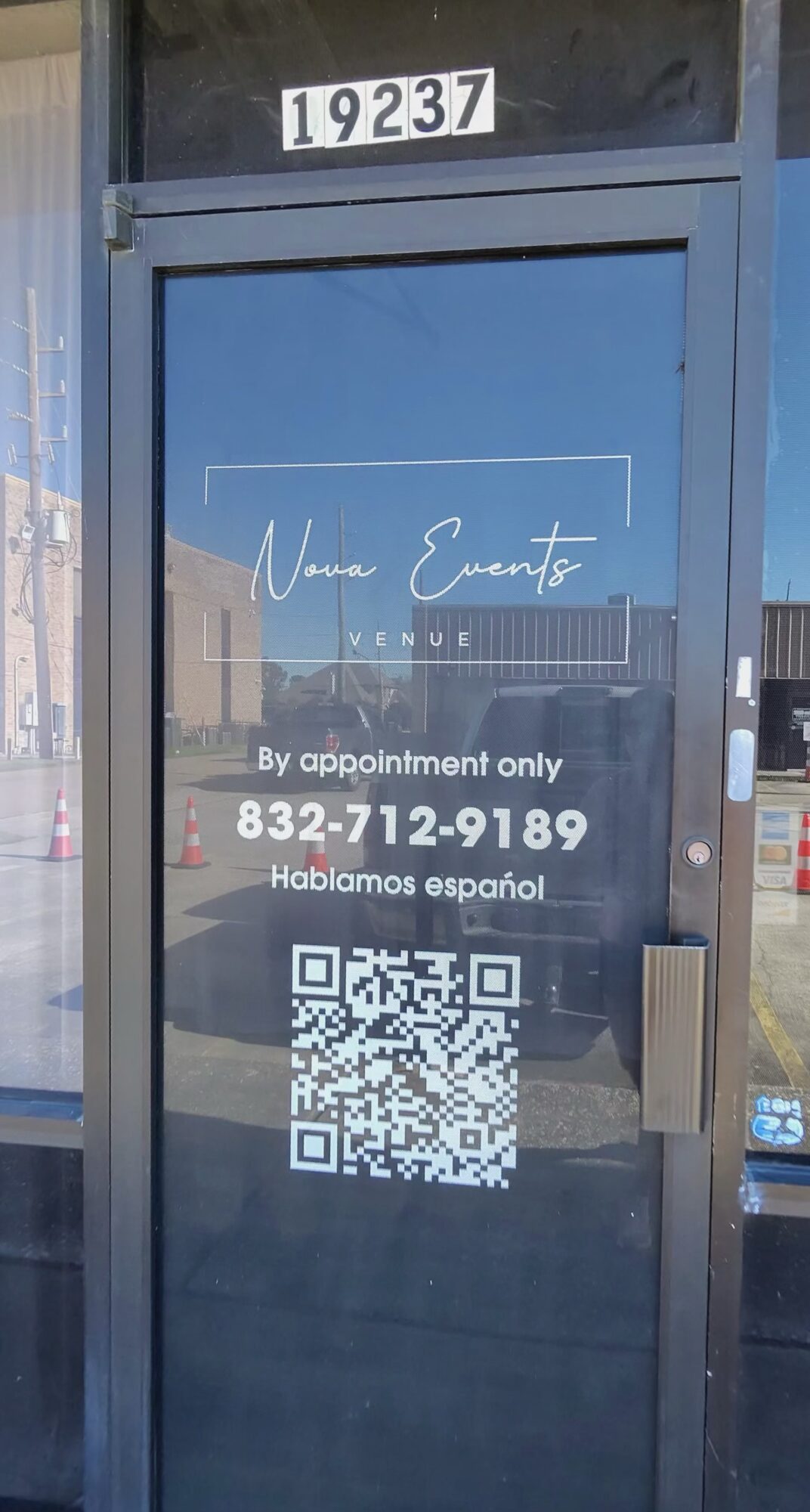 Glass door with a sign displaying a phone number, QR code, and text about appointment-only service, with a building reflection.