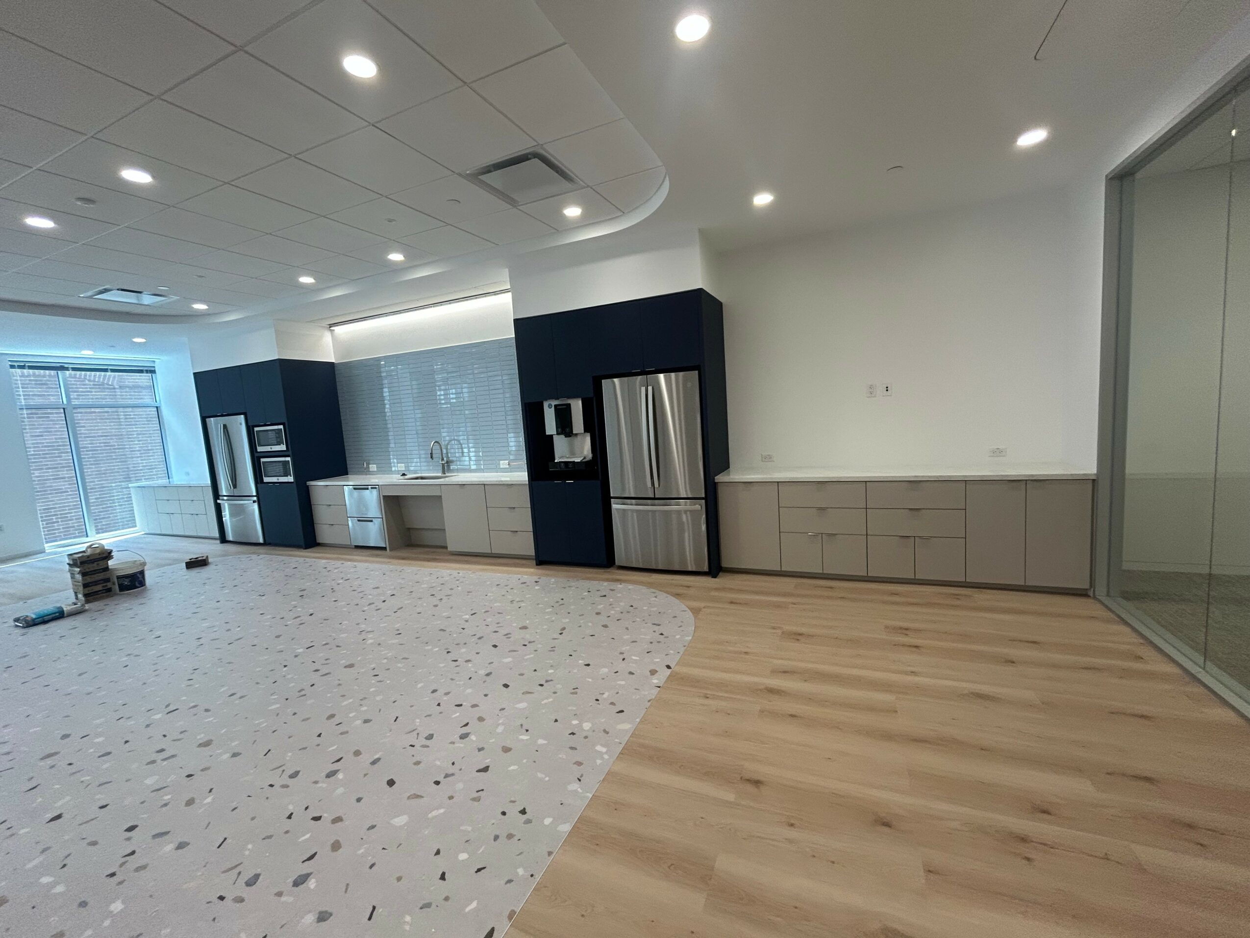 Modern interior space with mixed flooring, kitchen area, and large glass wall, well-lit with ceiling lights.