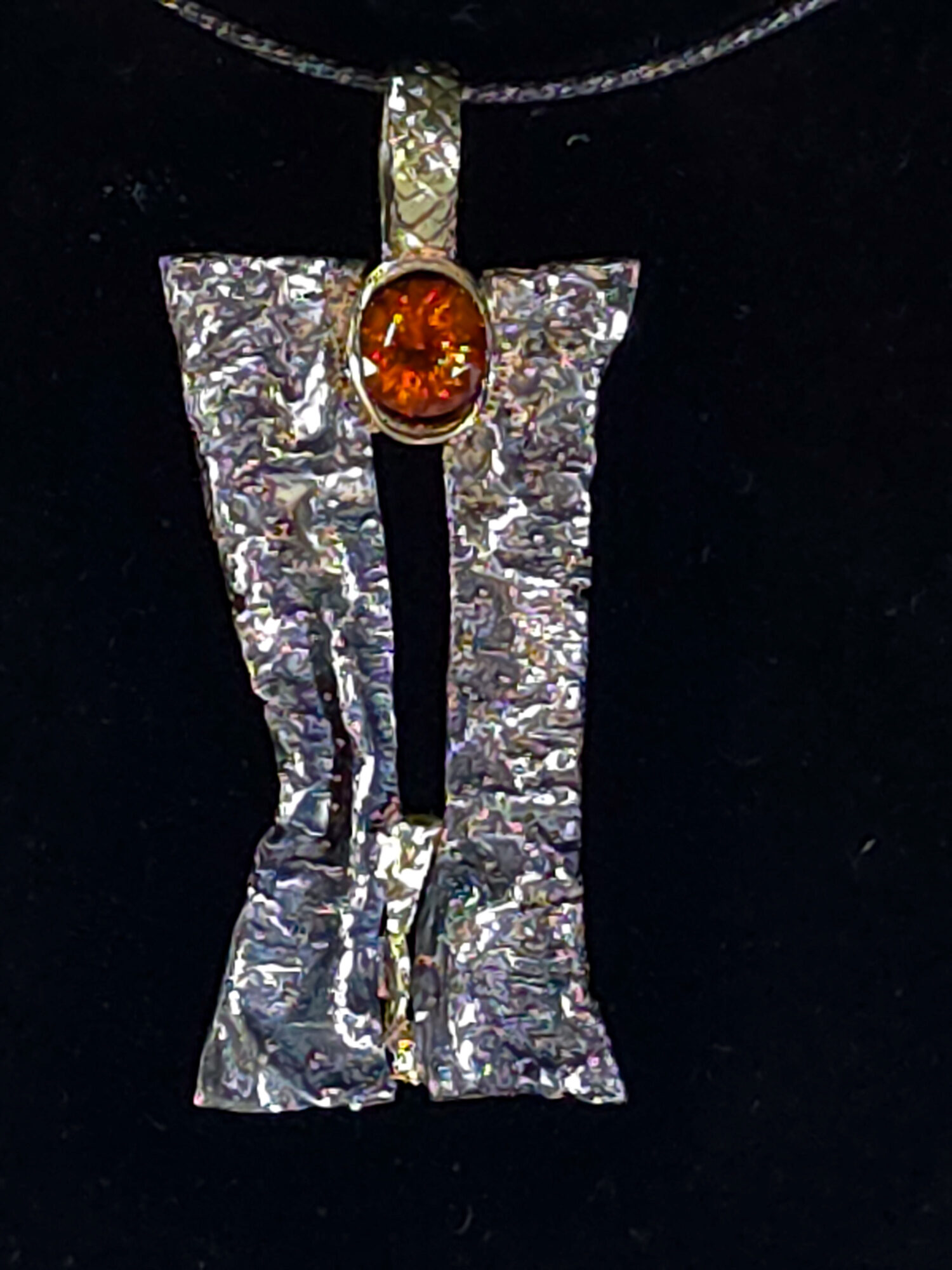 Pendant with a textured silver rectangular shape and an oval orange gemstone at the top, hanging from a chain.
