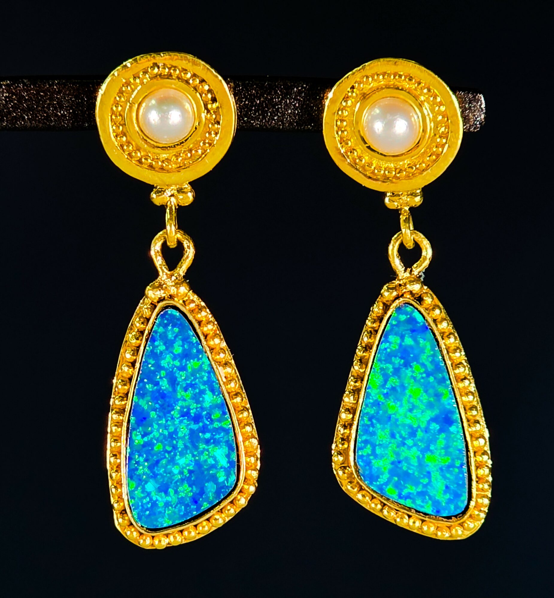 Gold earrings with pearl centers and blue-green irregular-shaped stones, hanging from a black background.